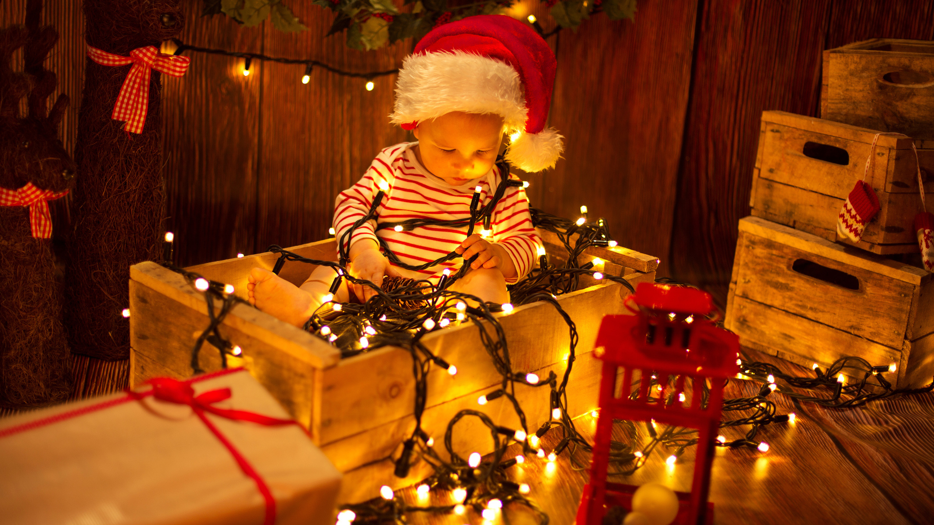 Маленький мальчик сидит в коробке с новогодней гирляндой