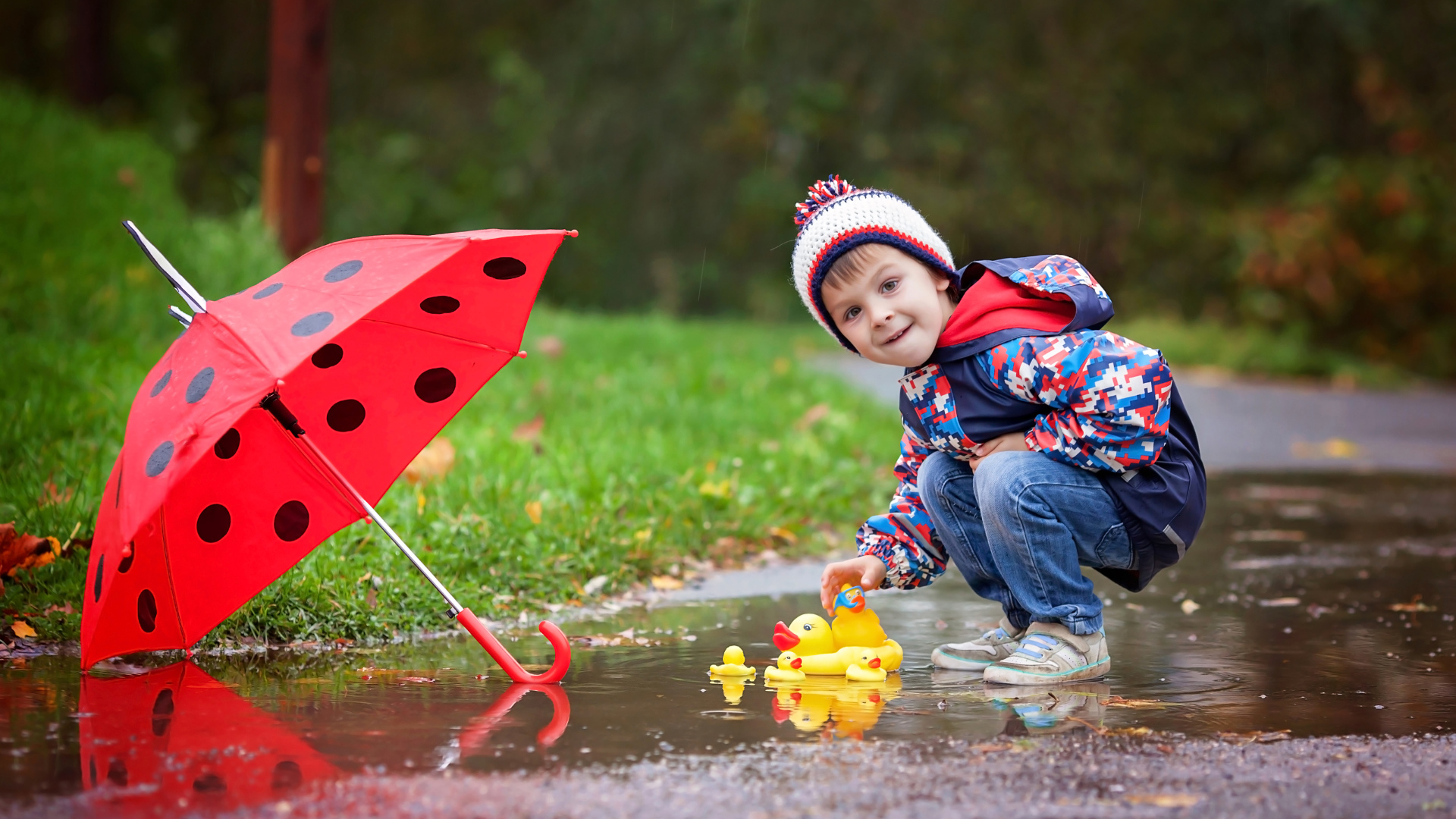 Маленький мальчик пускает резиновую уточку в лужу после дождя