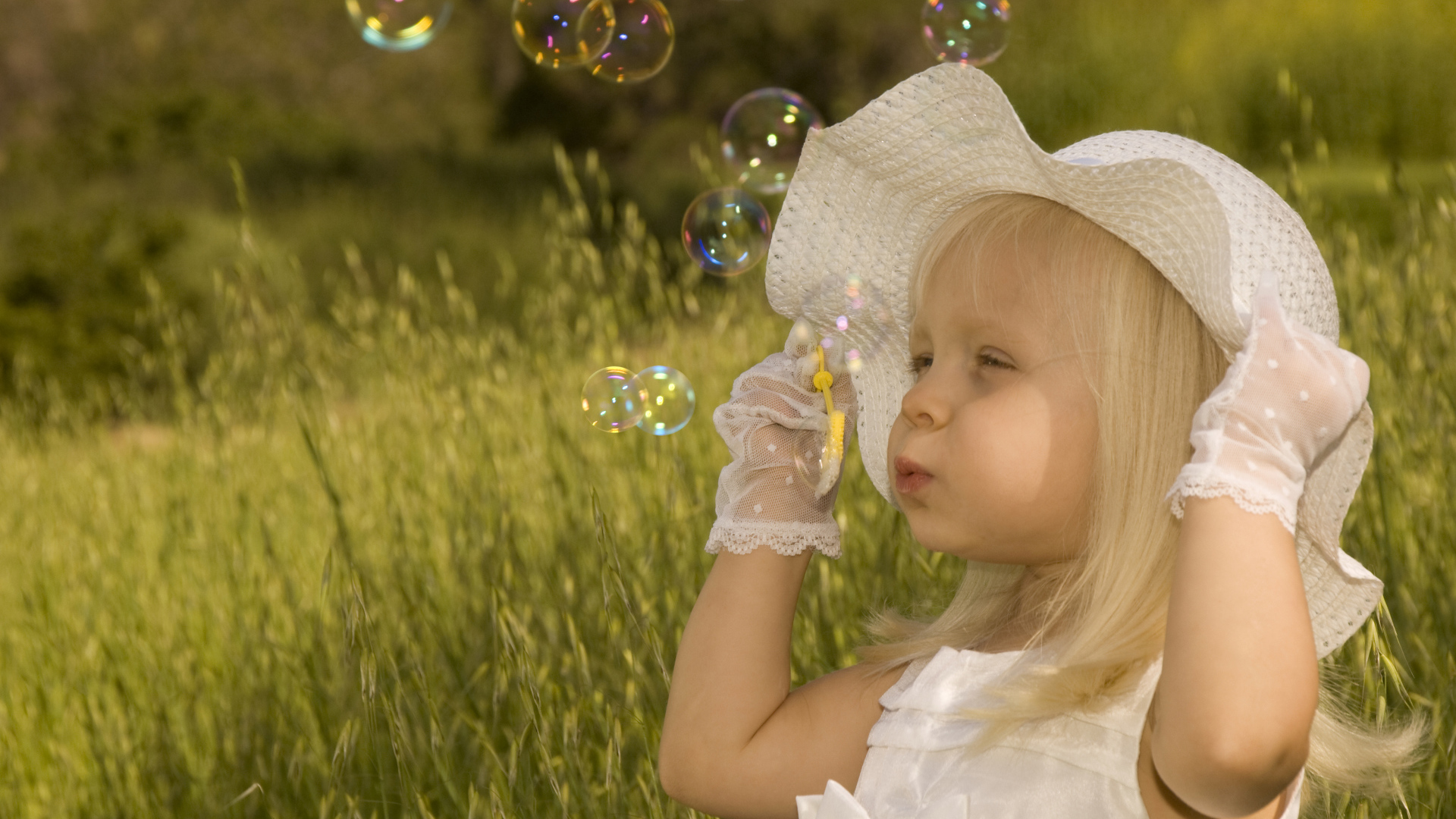 Маленькая девочка в большой белой шляпе пускает мыльные пузыри