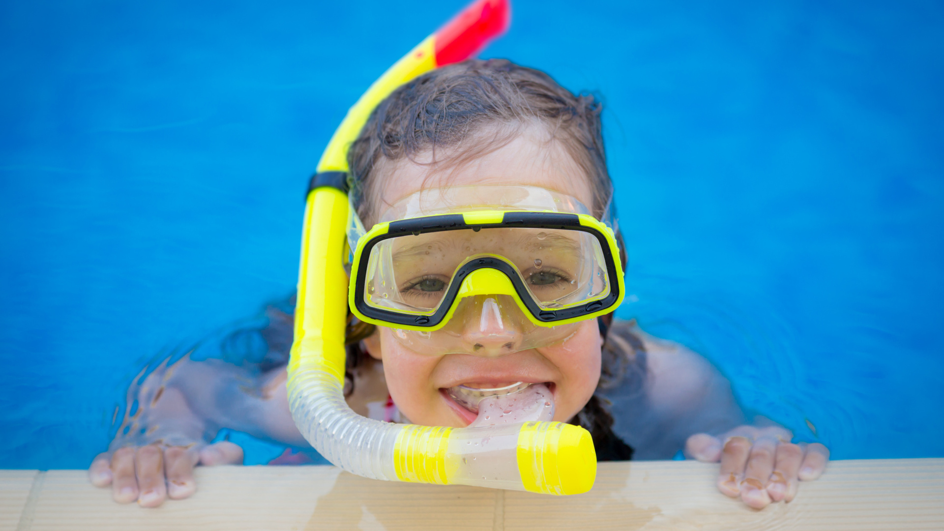 Маленькая девочка в маске с трубкой плавает в бассейне