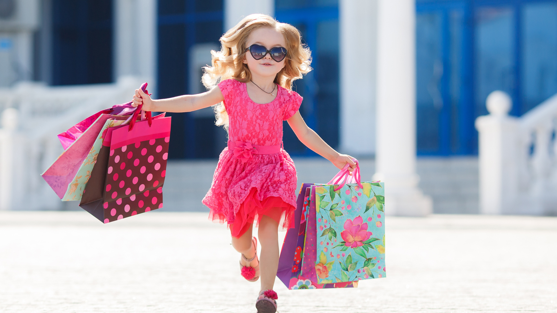 Маленькая девочка в розовом платье бежит с покупками из магазина