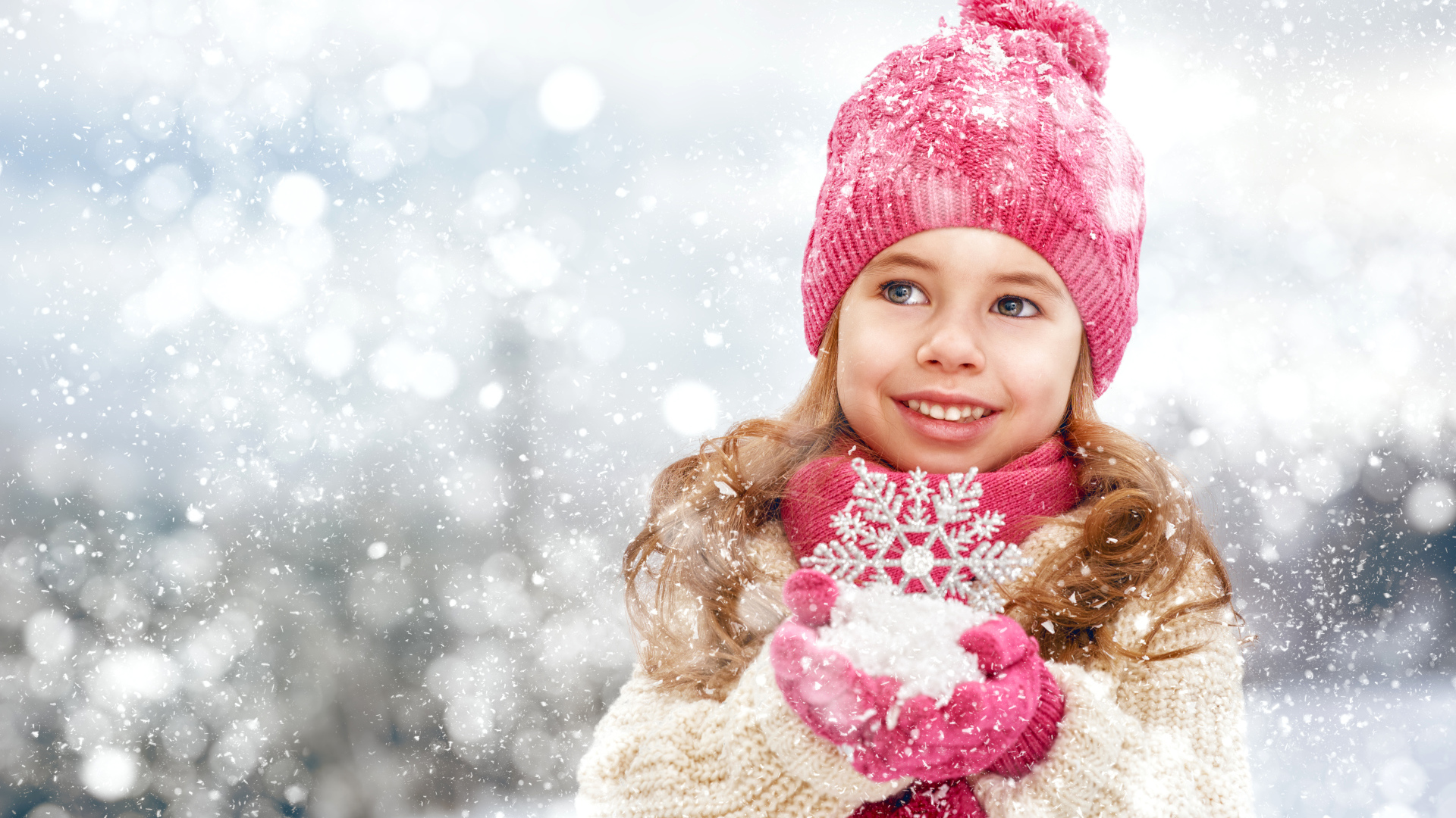 Маленькая девочка в зимней одежде держит снег в руках