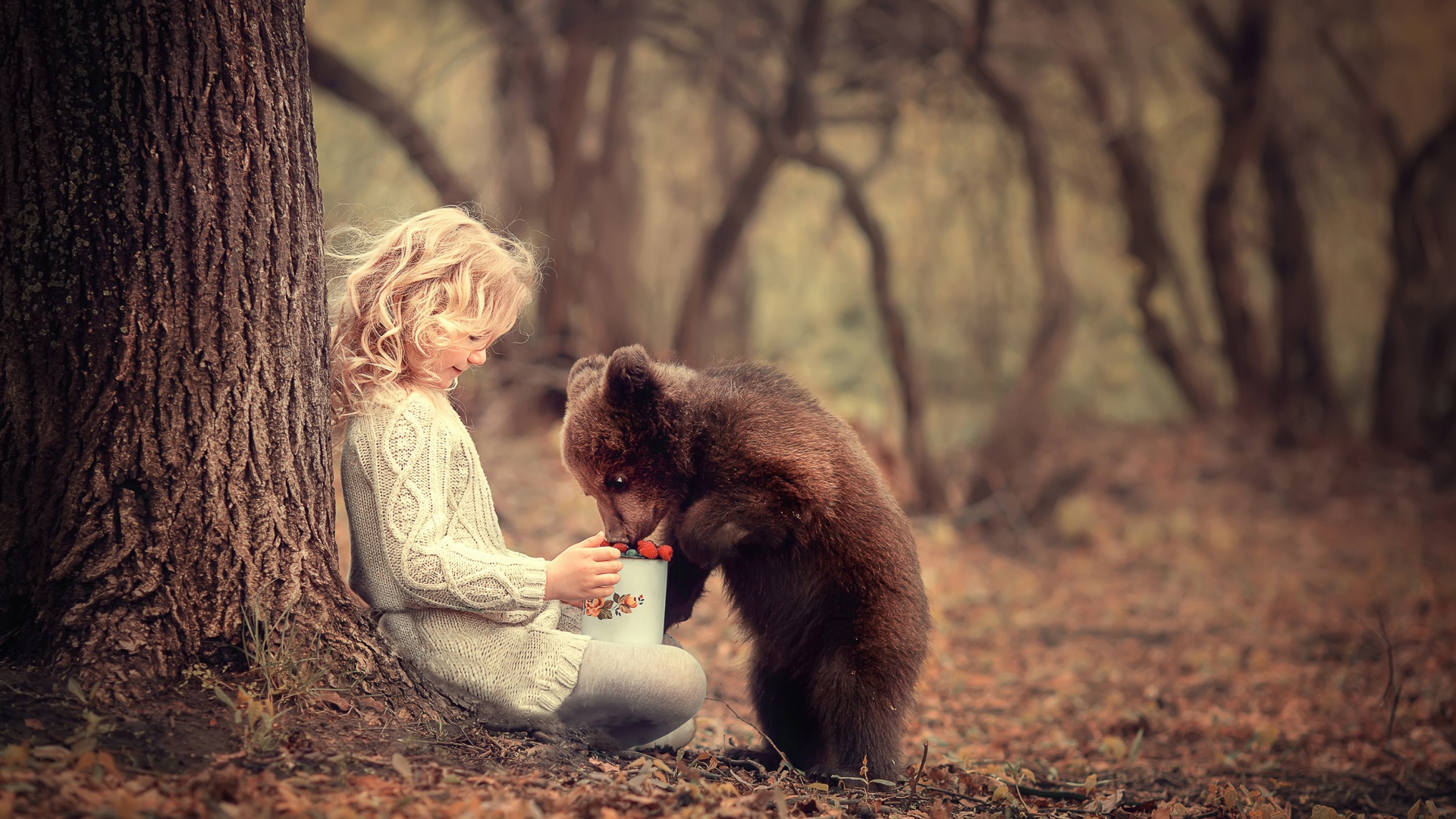 Маленькая девочка сидит у дерева с медвежонком гризли