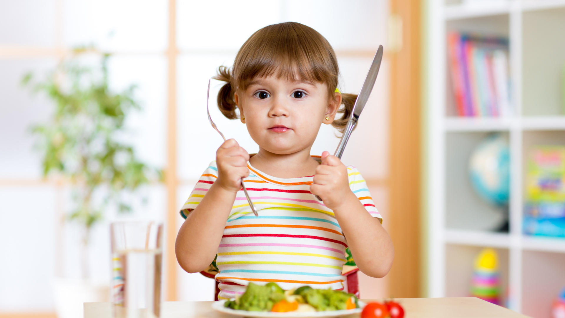 Маленькая девочка со столовыми приборами и тарелкой