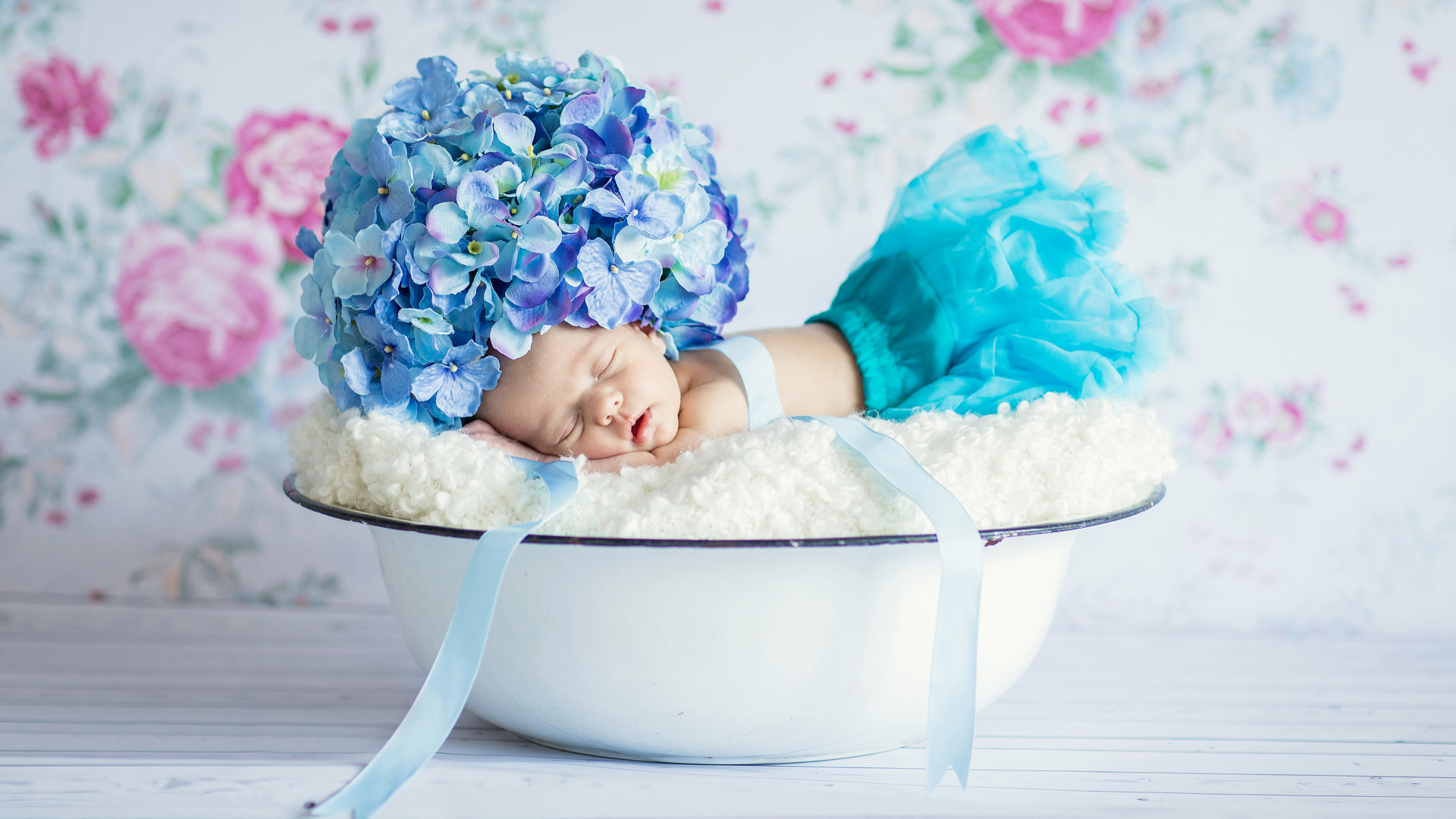 Маленький грудной ребенок спит в миске с шапкой из цветов гортензии на голове