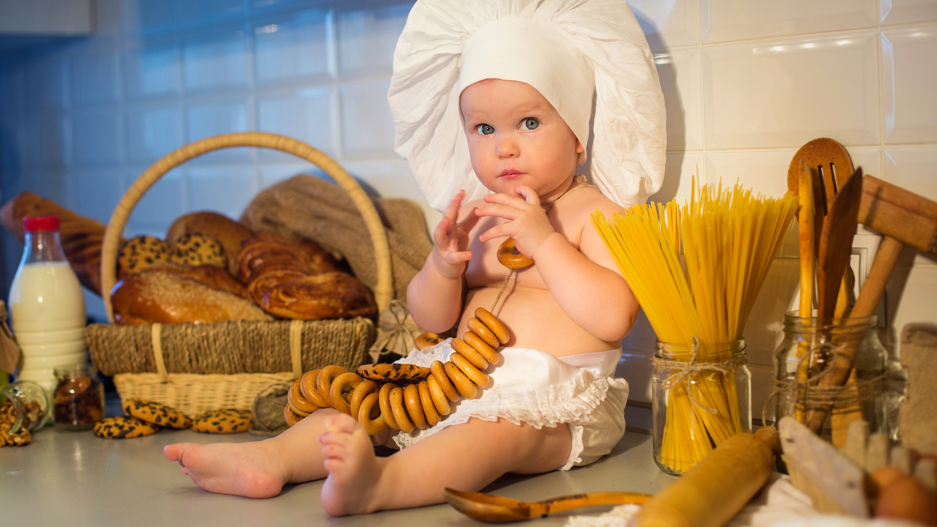Маленький ребенок в шапке повара сидит на столе с выпечкой