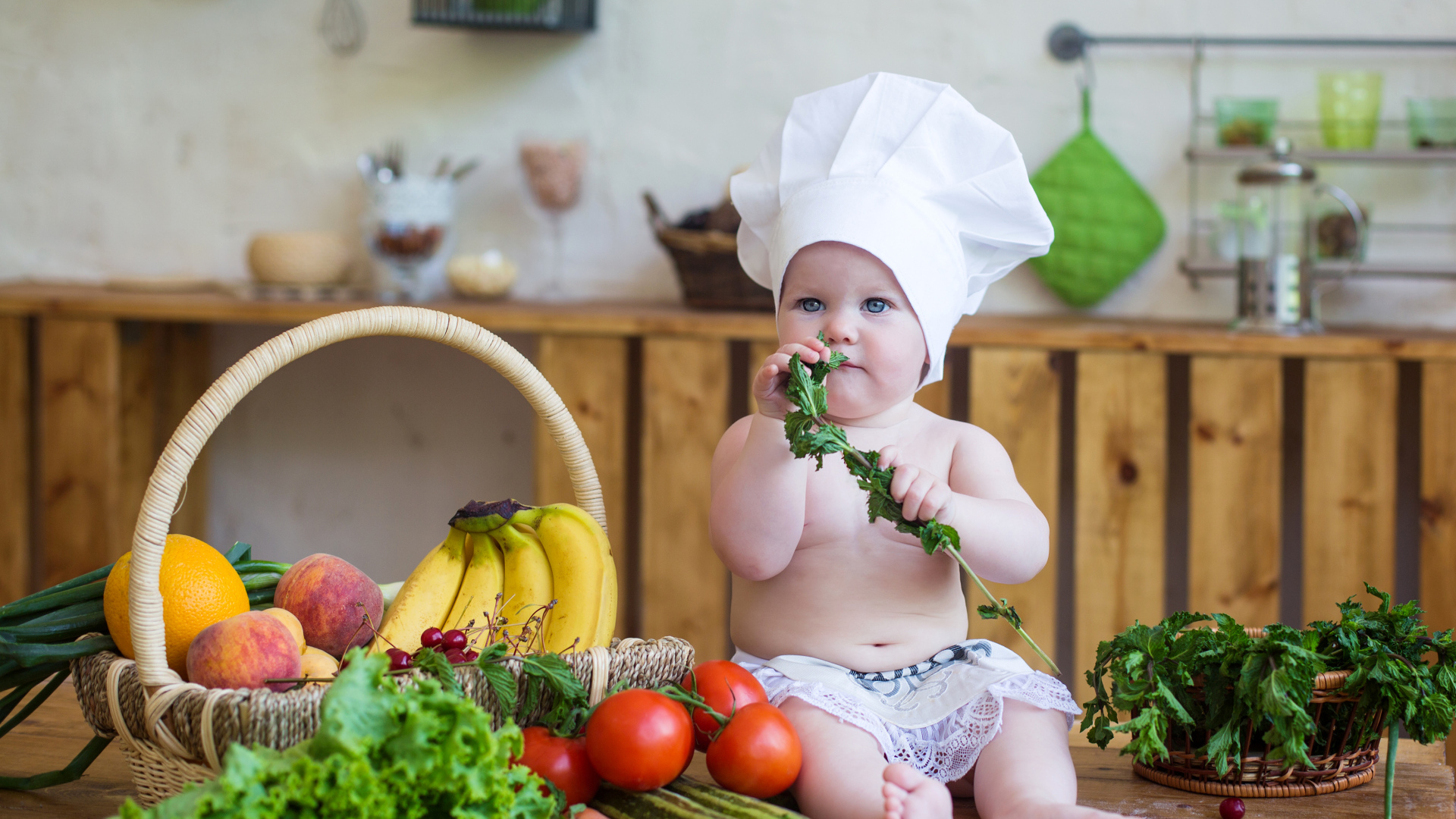 Маленький ребенок в шапке повара сидит на столе с овощами