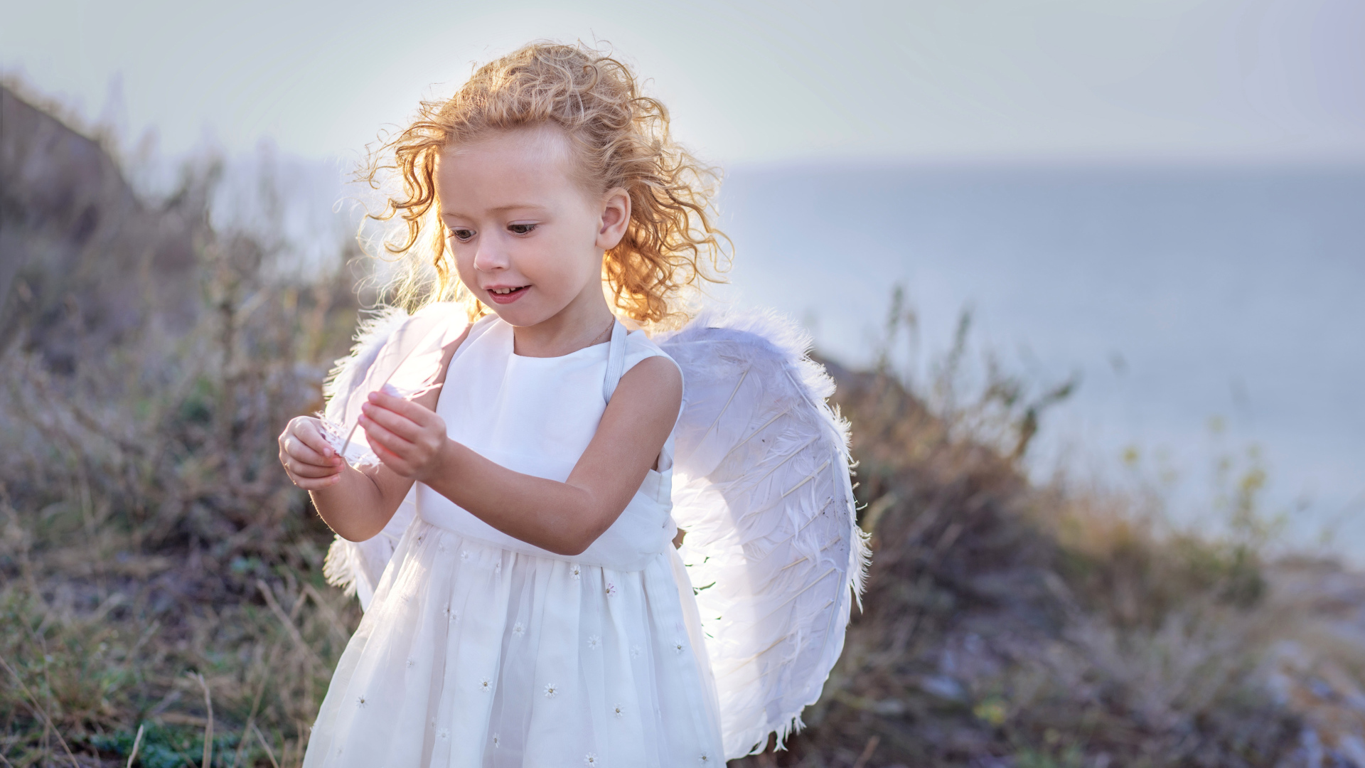 Красивая маленькая девочка в белом платье с крыльями ангела