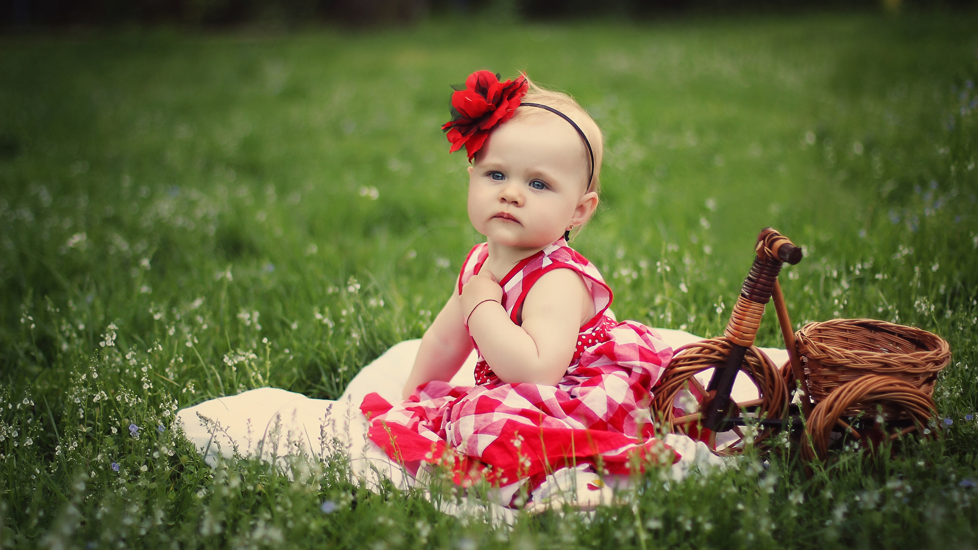 Красивая маленькая девочка с красным цветком на голове сидит на зеленой траве