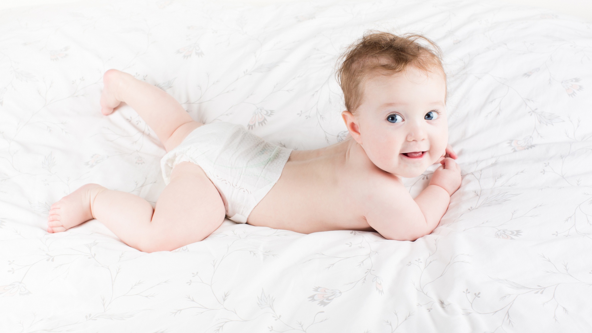 Забавный голубоглазый малыш лежит на белом покрывале