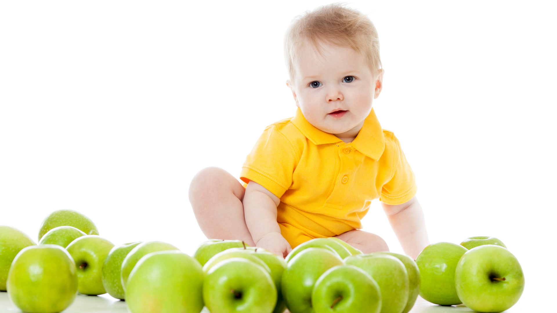 Маленький мальчик с зелеными яблоками на белом фоне