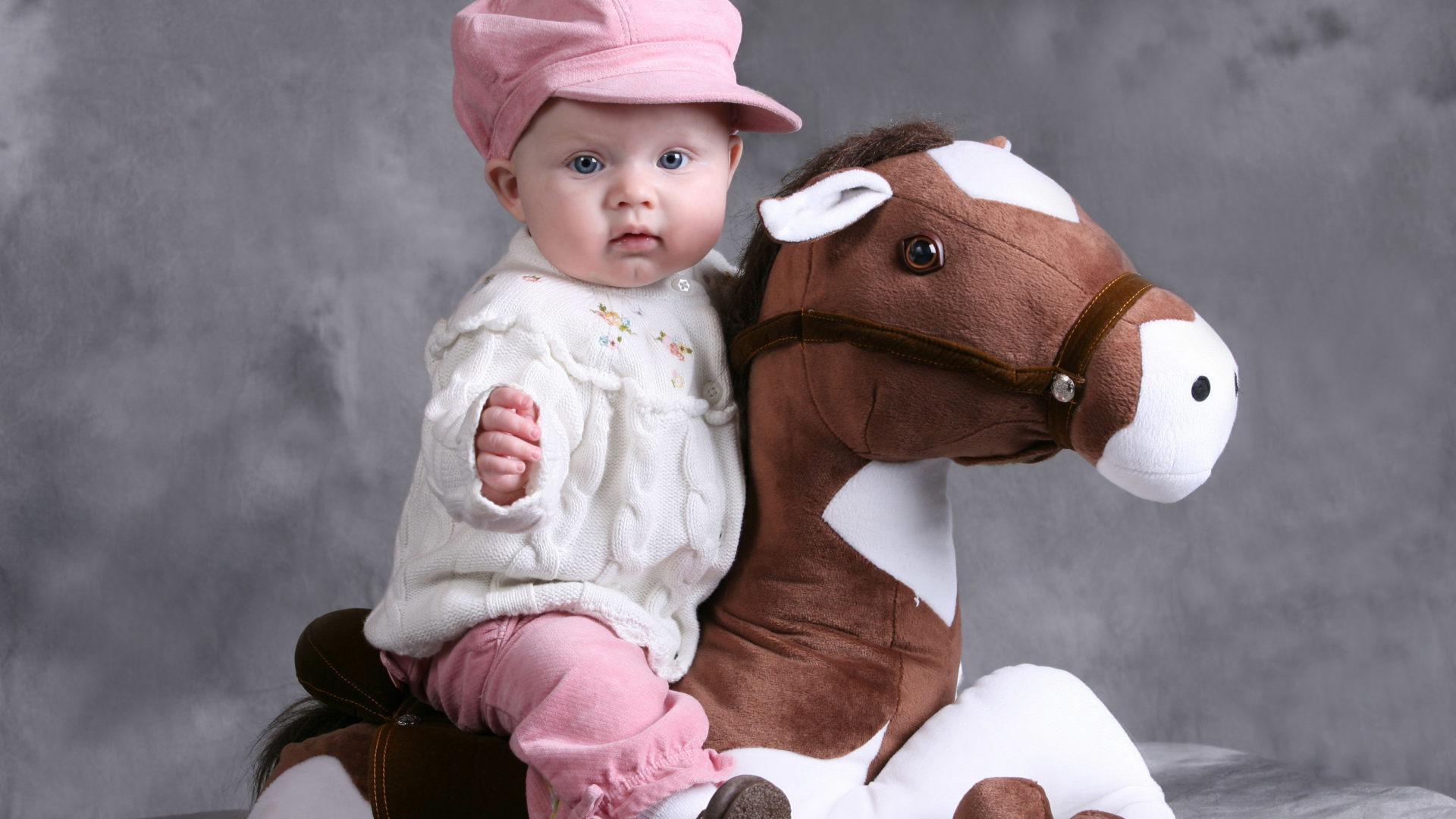 Маленькая девочка в розовой кепке сидит на игрушечной лошади