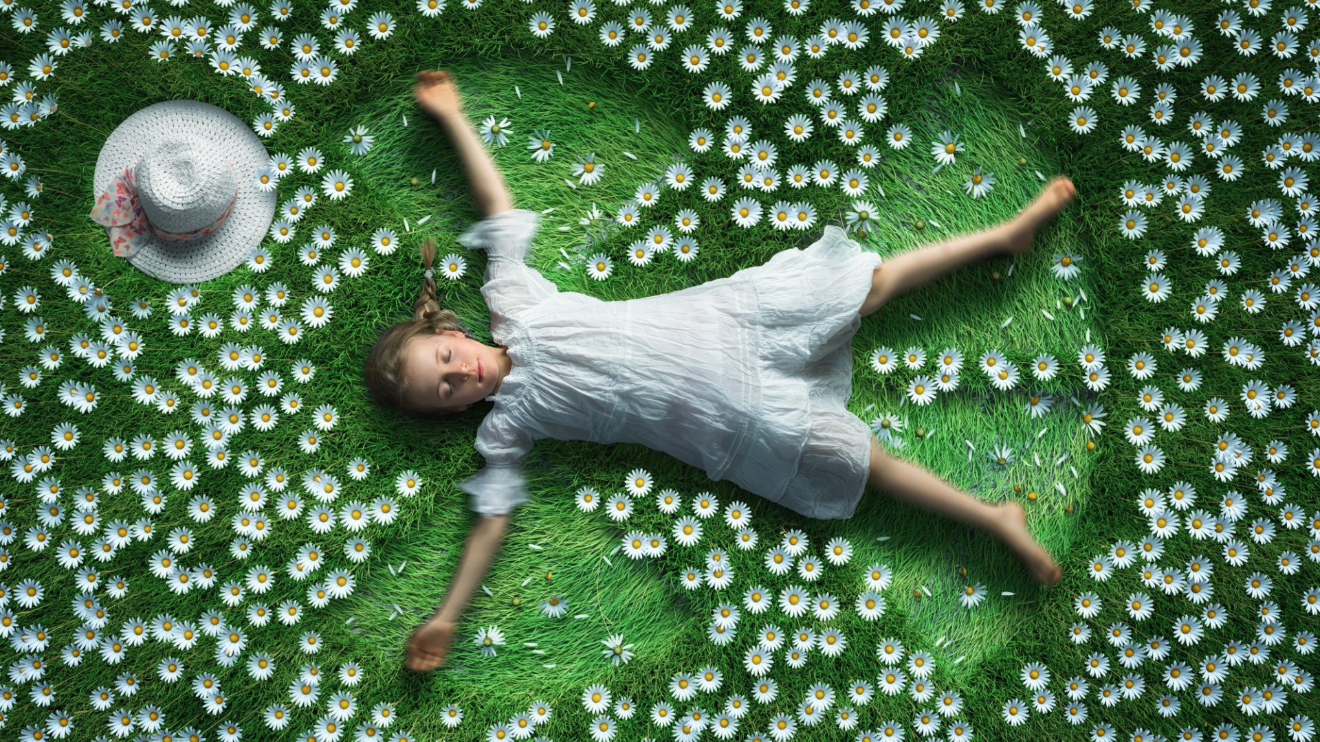 Маленькая девочка в белом платье лежит на зеленой траве с ромашками