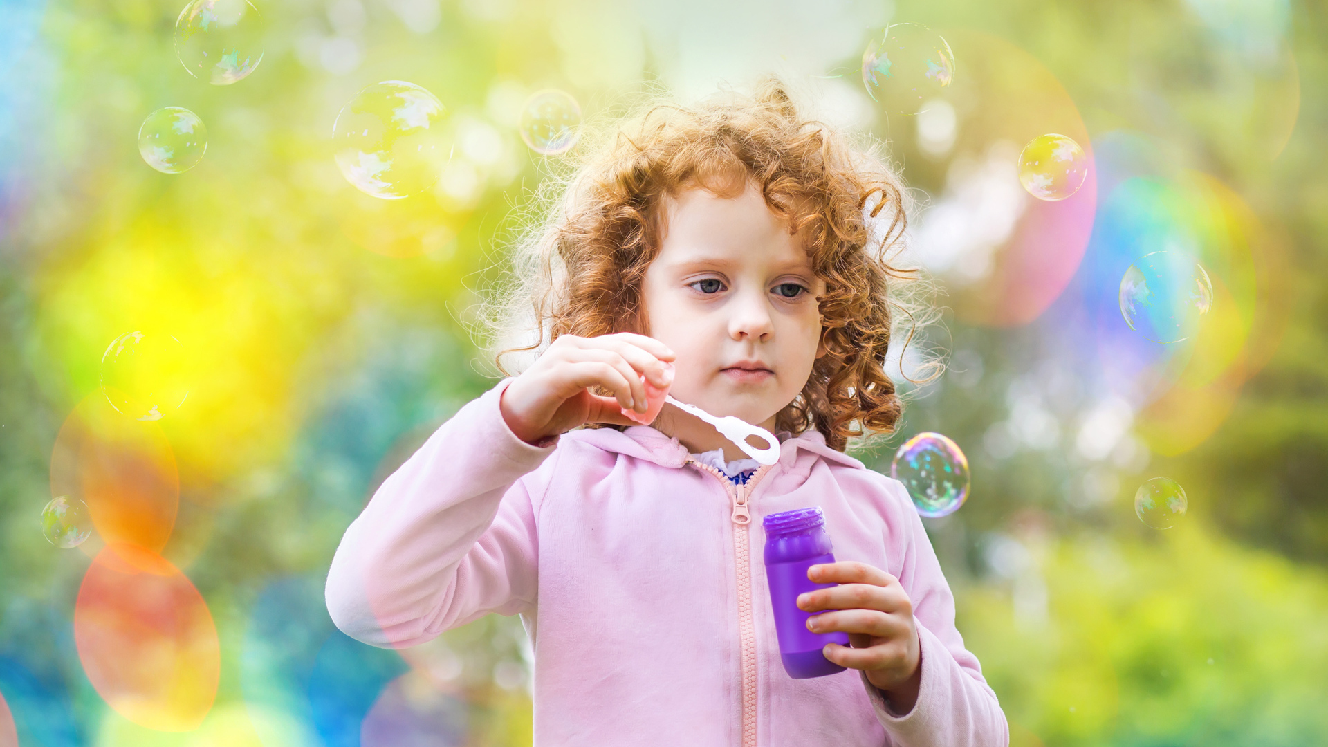 Маленькая рыжеволосая кудрявая девочка с мыльными пузырями