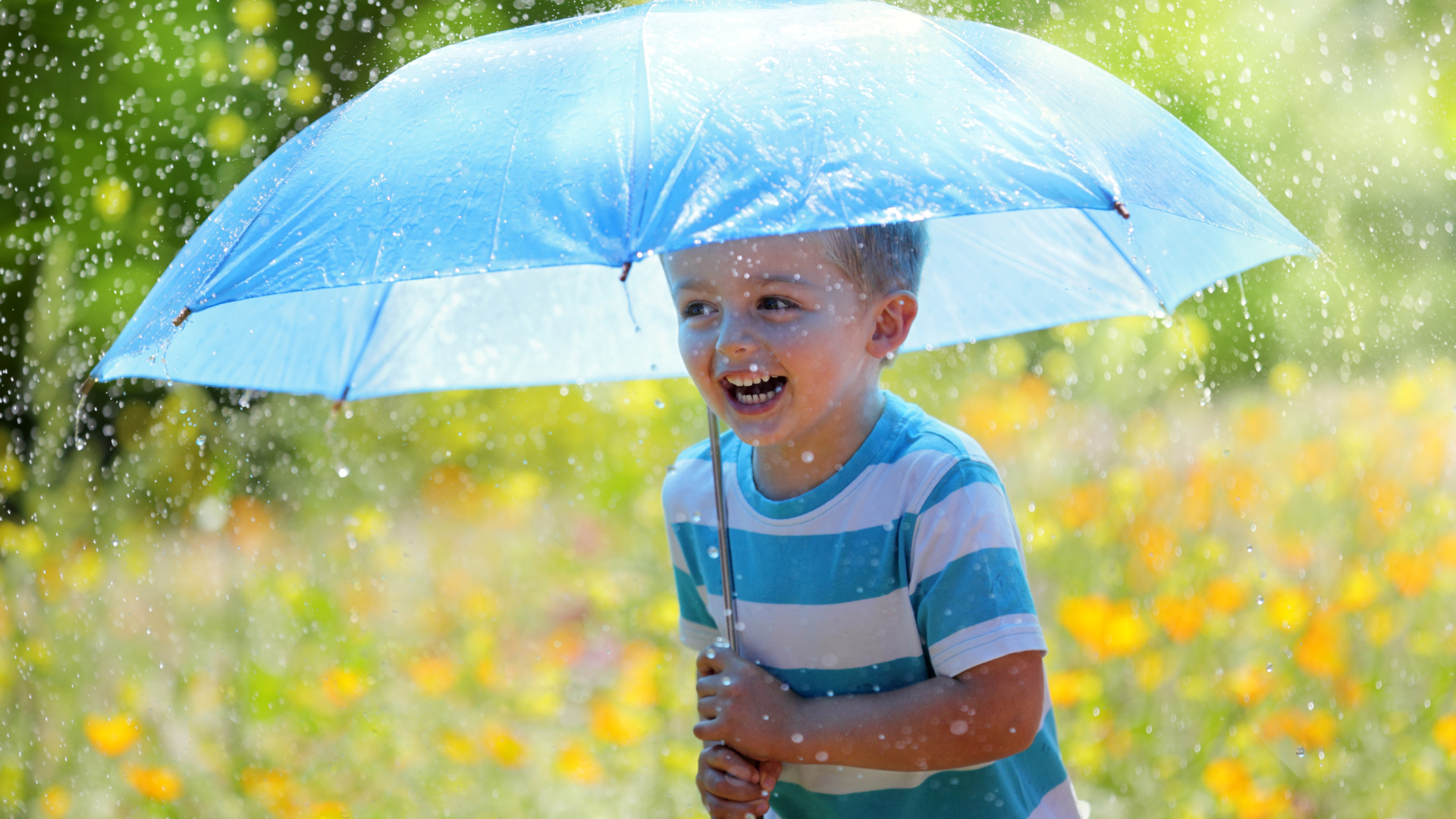 Маленький улыбающийся мальчик с голубым зонтом под дождем