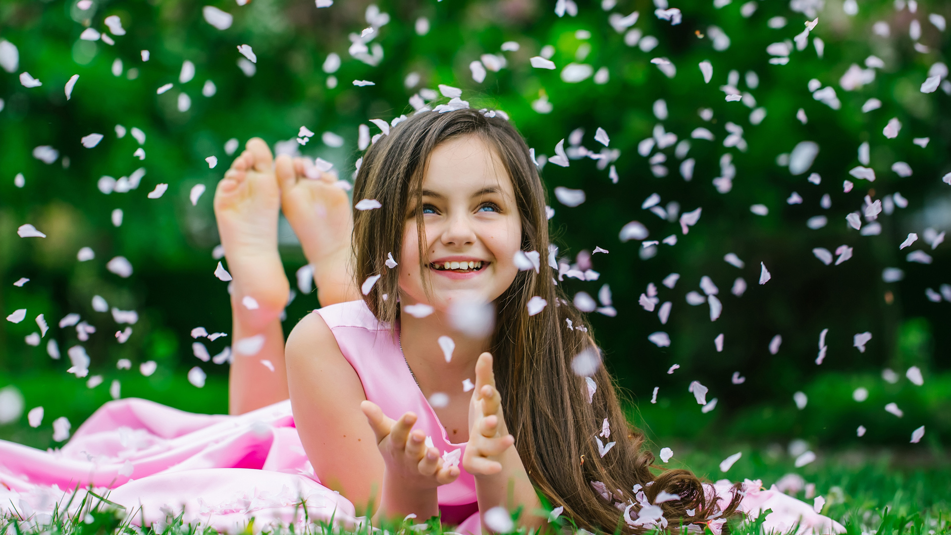 Маленькая улыбающаяся девочка шатенка ловит лепестки