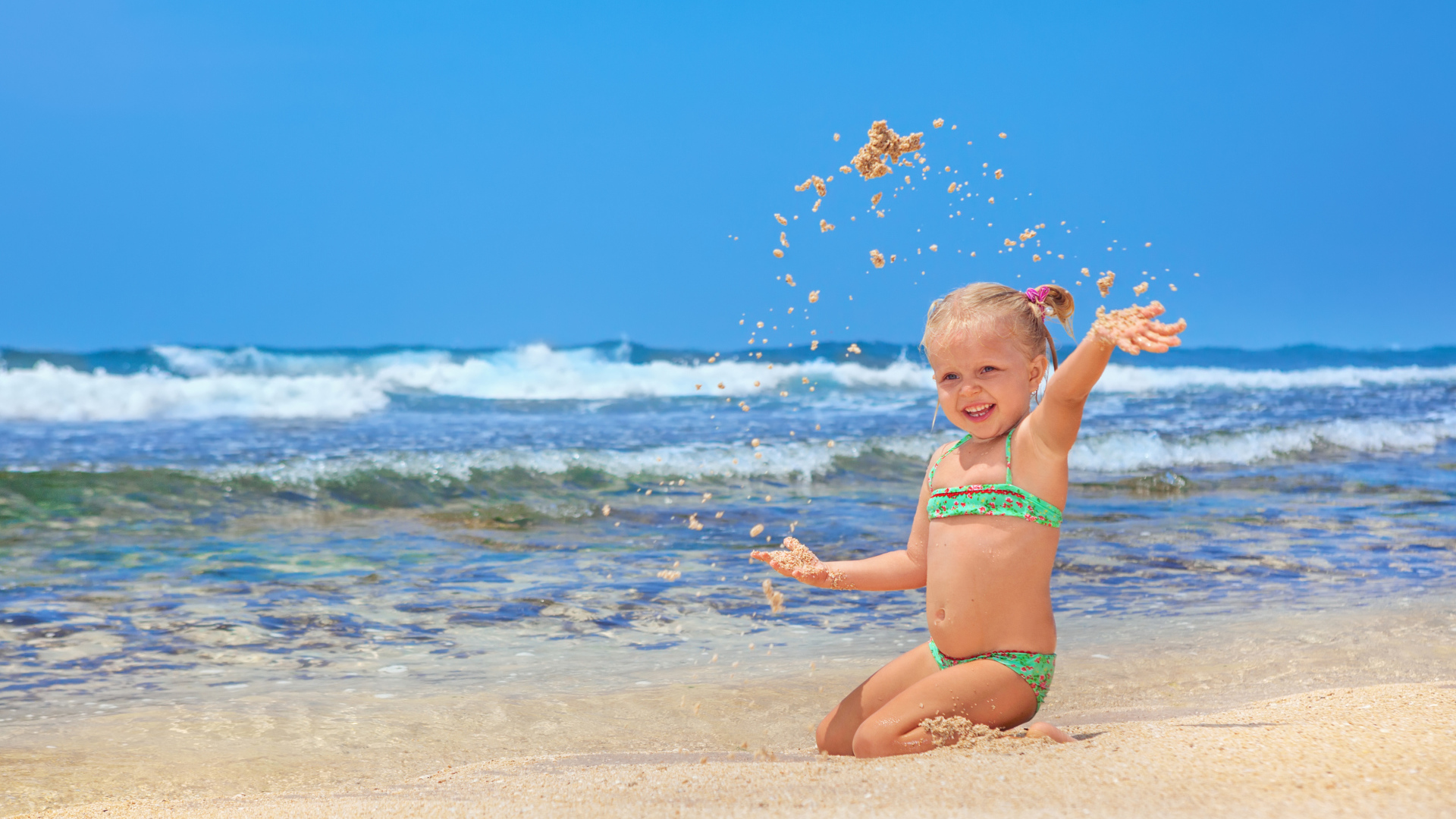 Маленькая улыбающаяся девочка играет на пляже с песком