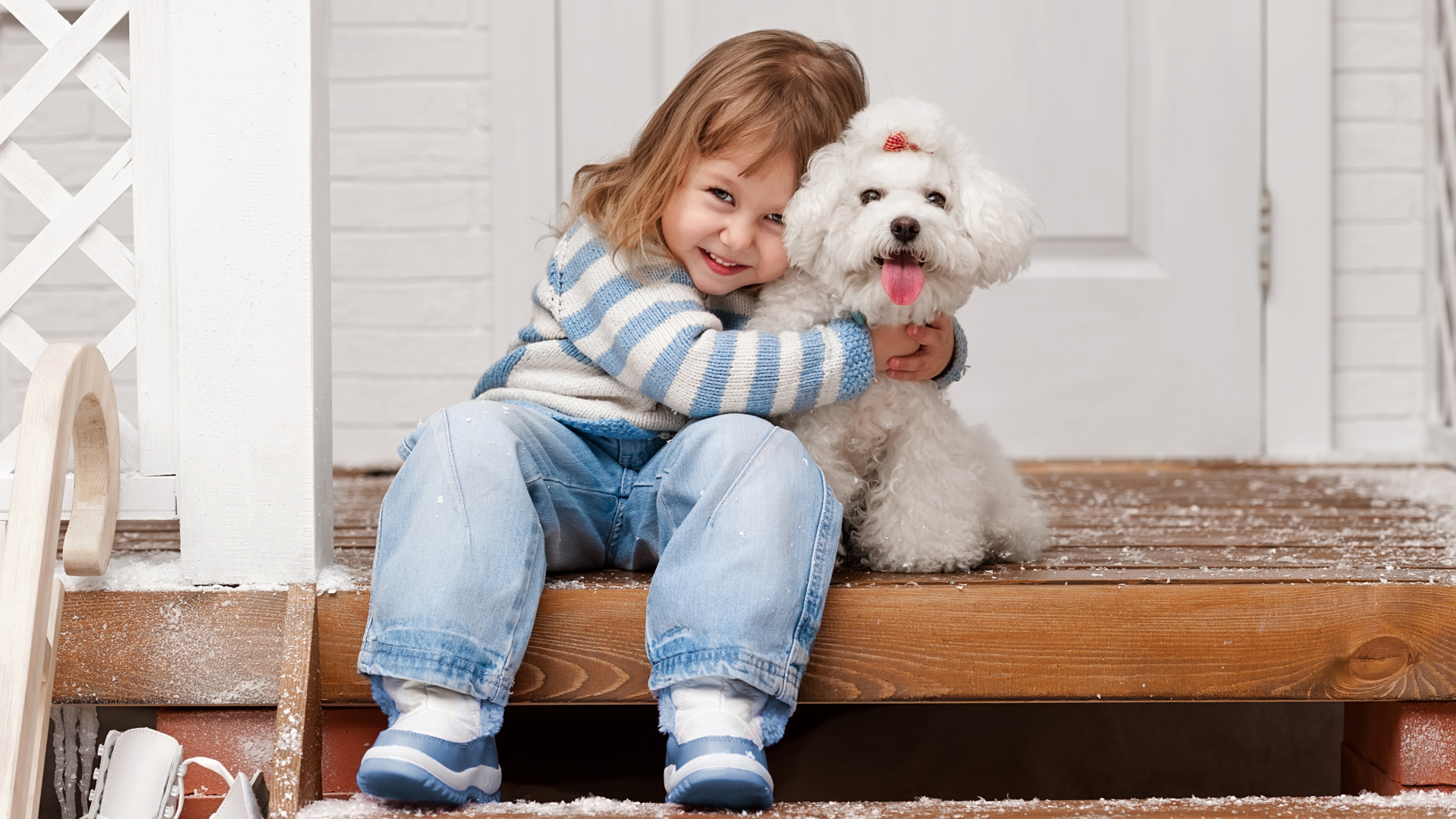 Маленькая улыбающаяся девочка сидит с белым пуделем на ступеньках