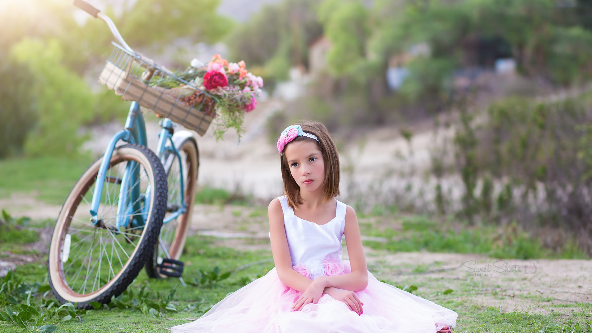 Грустная девочка в красивом платье сидит на траве с велосипедом