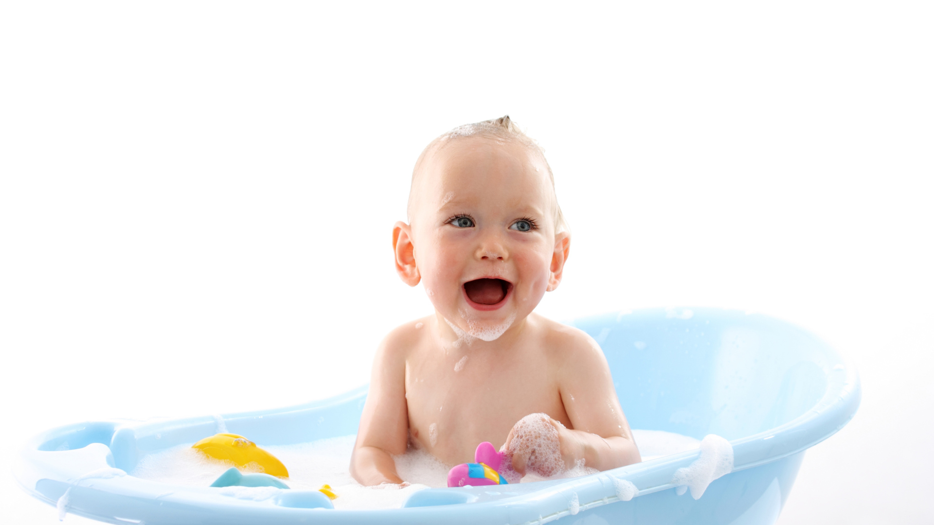 Улыбающийся грудной ребенок сидит в синей ванночке на белом фоне
