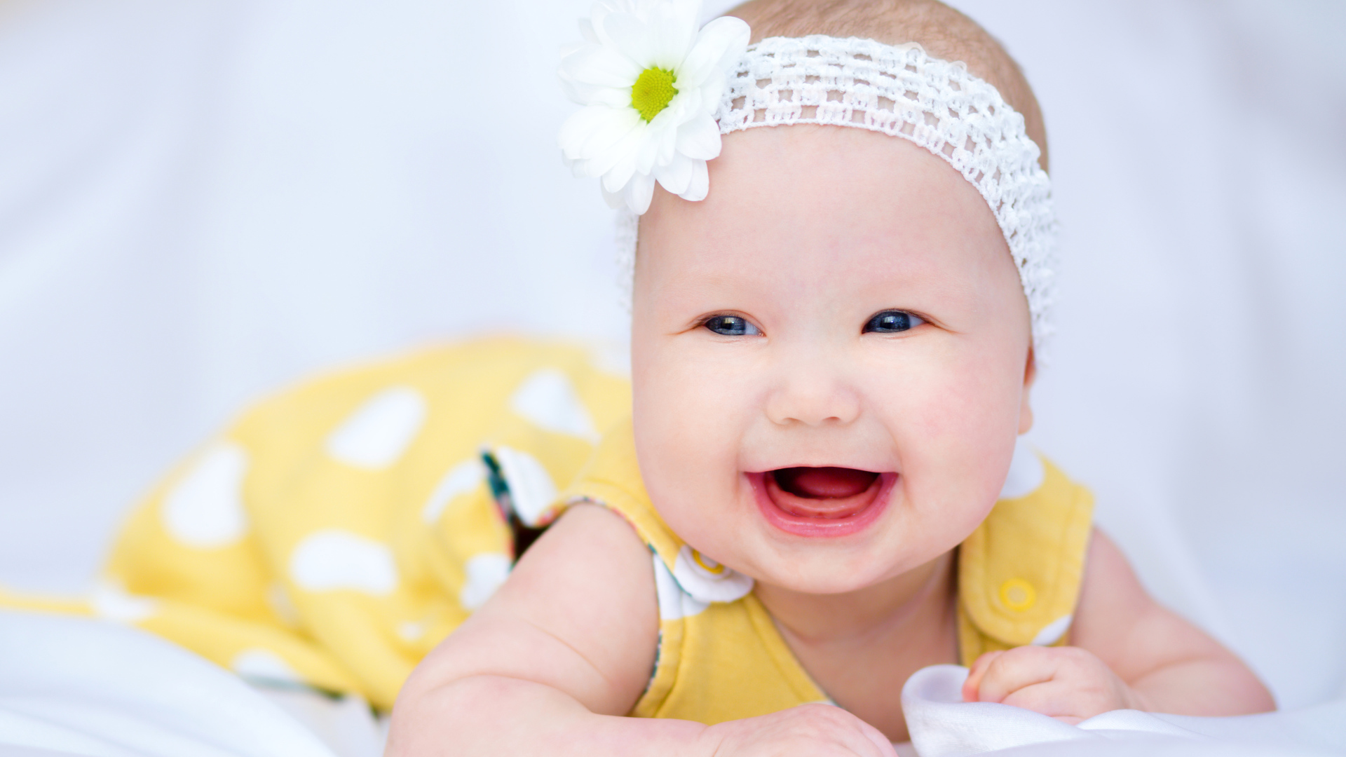 Улыбающаяся маленькая девочка в повязке с белым цветком на голове