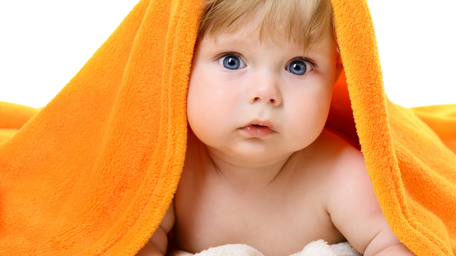 Голубоглазый малыш лежит под оранжевым покрывалом