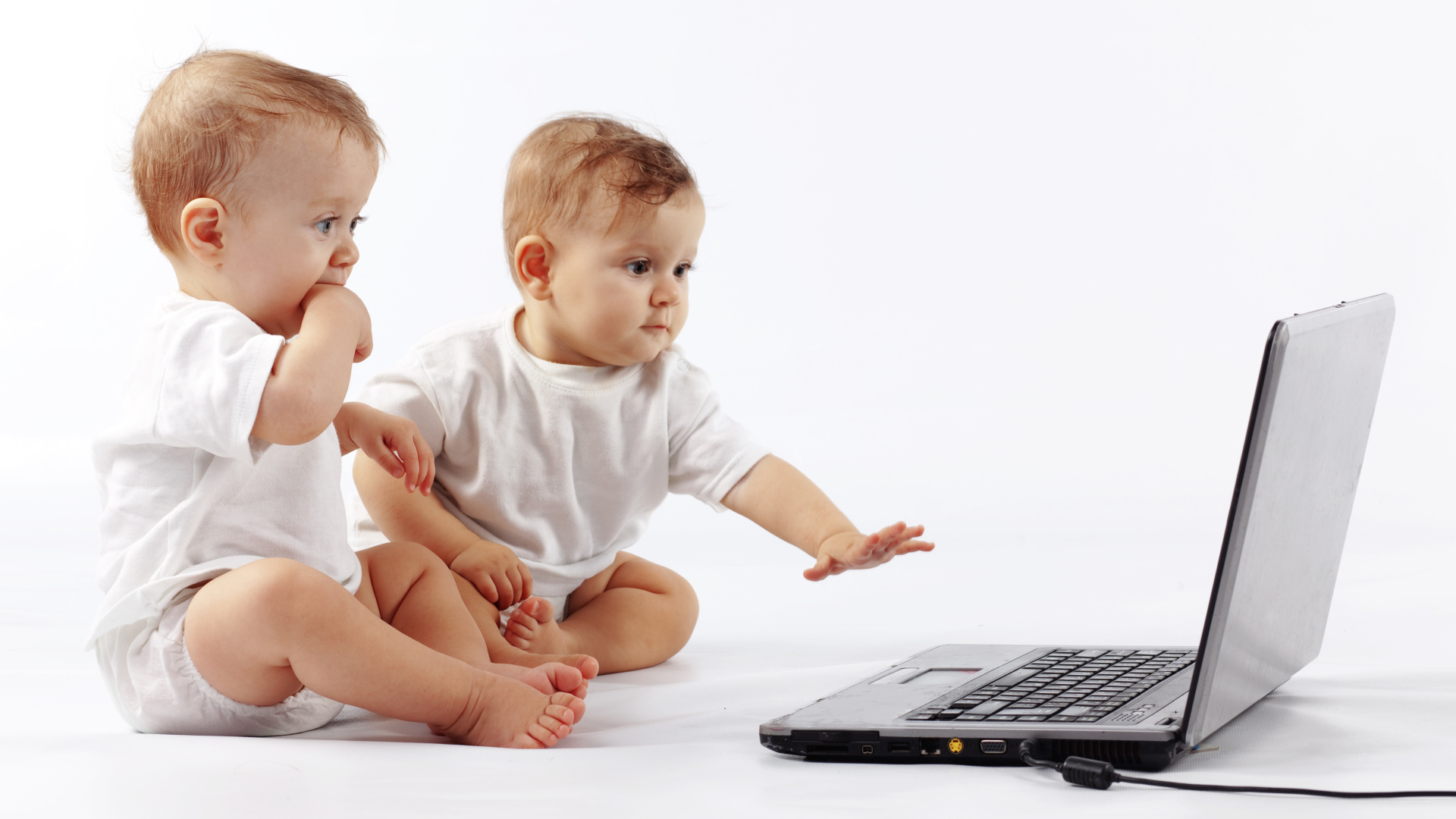 Два младенца перед ноутбуком на белом фоне