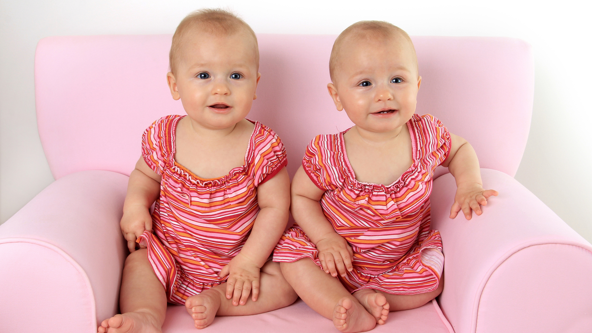 Две милые маленькие девочки сидят на розовом диване