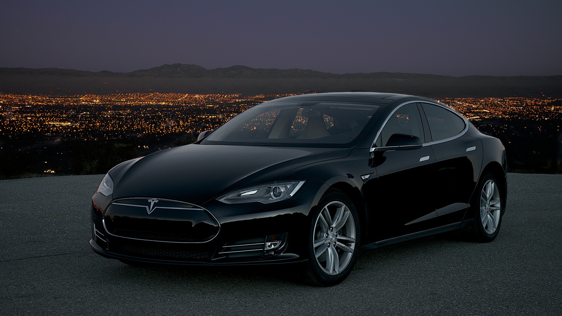 Черный стильный электромобиль Tesla Model S на фоне ночного мегаполиса 
