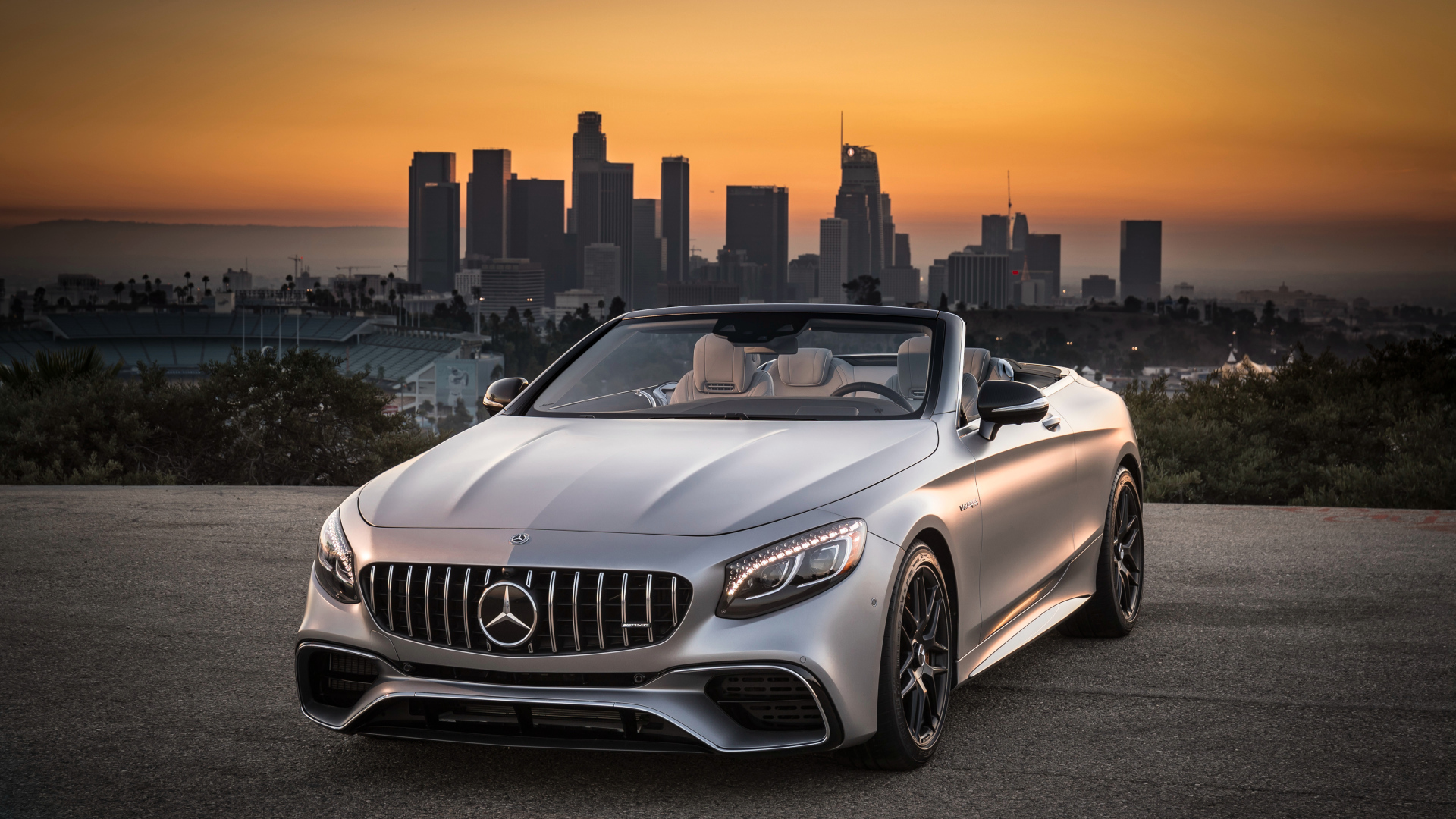 Серебристый автомобиль Mercedes AMG S63 4MATIC Cabriolet, 2018 на фоне мегаполиса