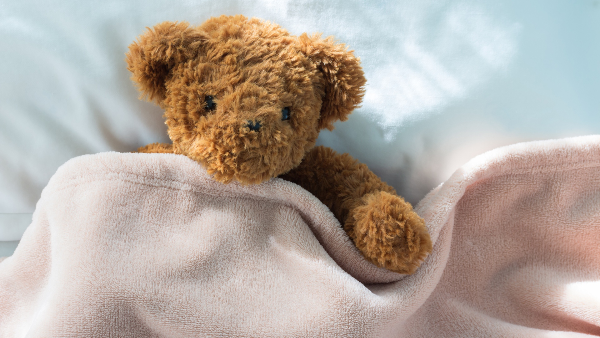 Плюшевый медведь в кровати под одеялом