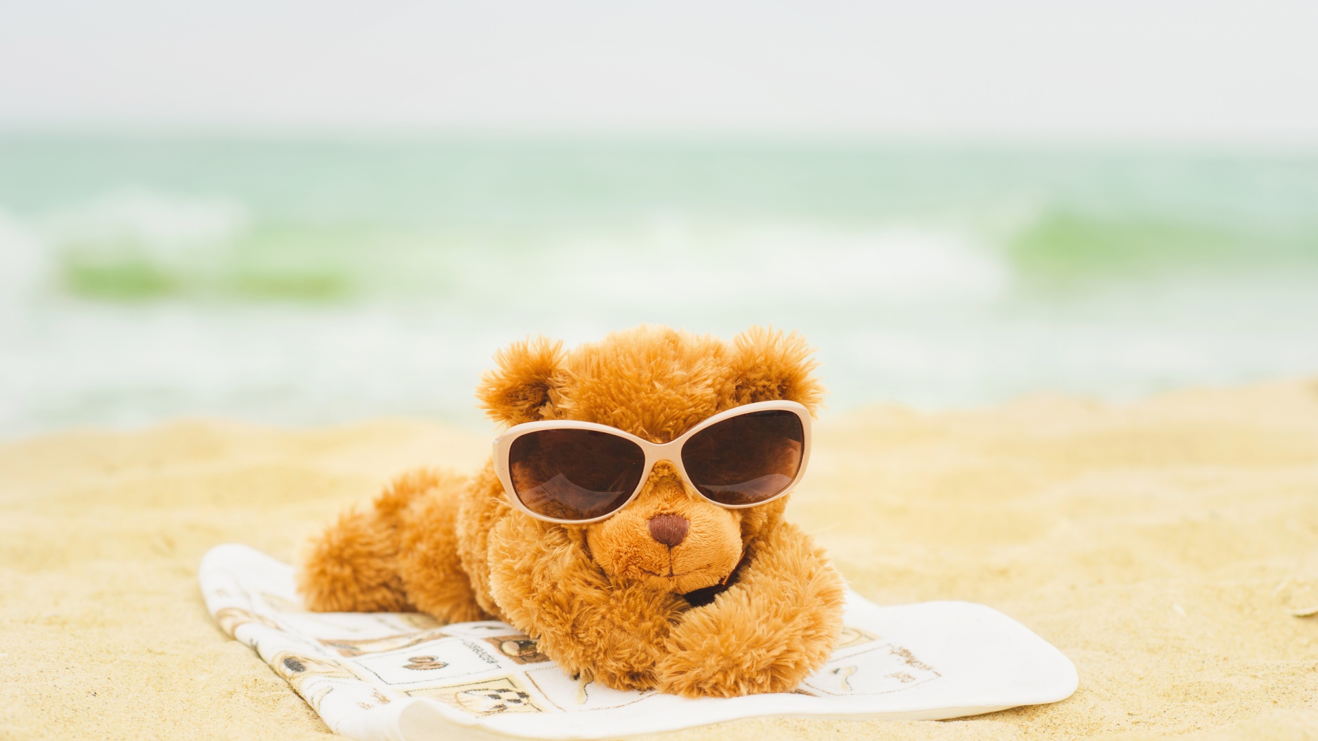 Плюшевый мишка в солнечных очках лежит на пляже