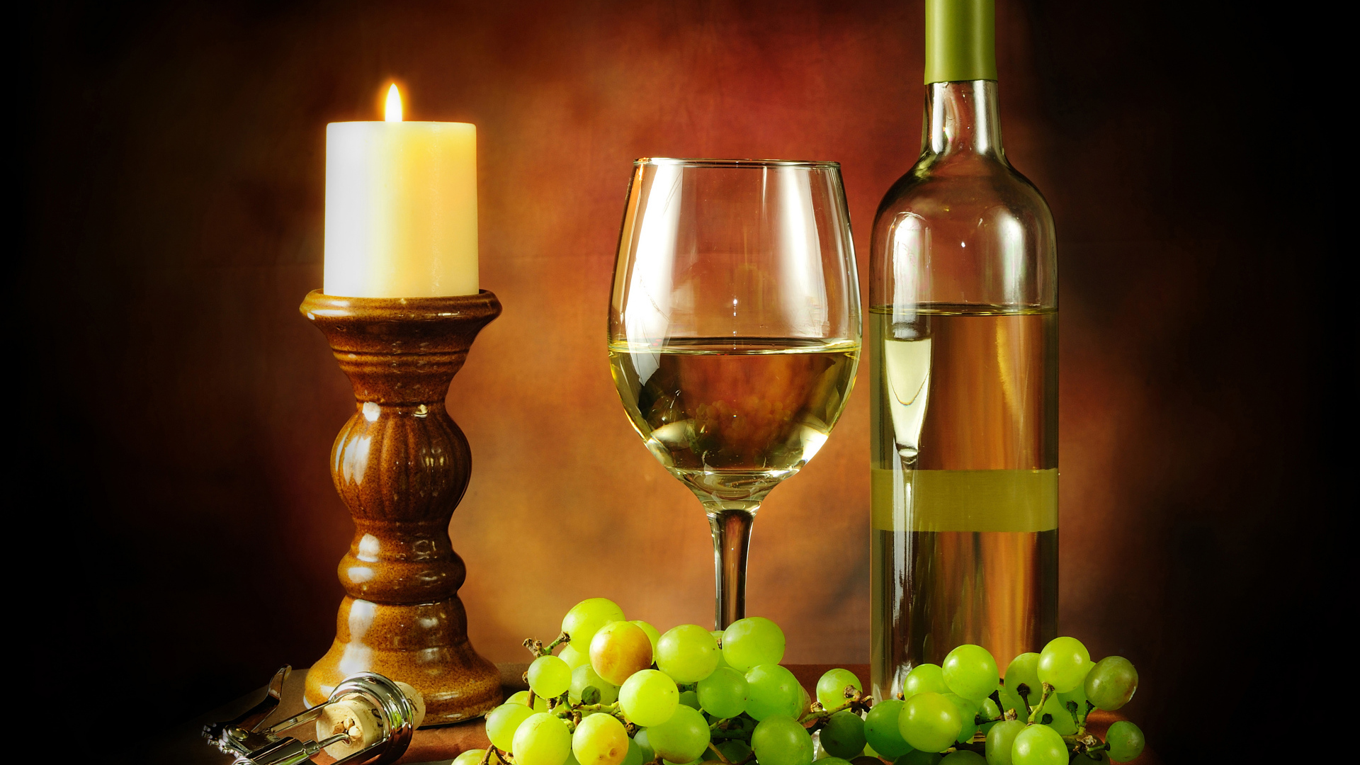 Бутылка белого вина на столе со свечей, белым виноградом и бокалом 