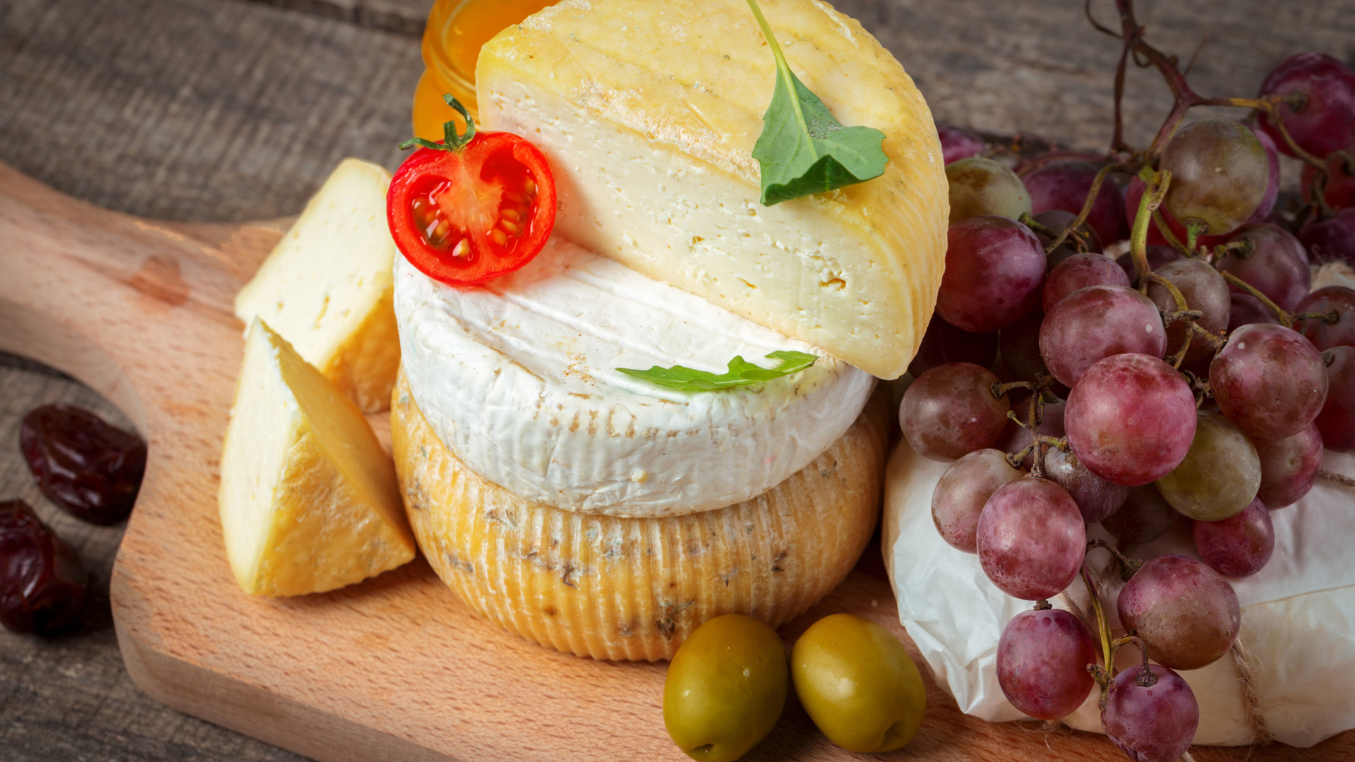 Сыр на разделочной доске с виноградом и оливками