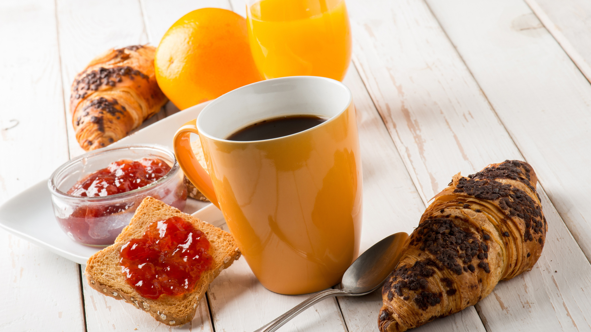 Coffee on a wooden table with croissants, juice and jam