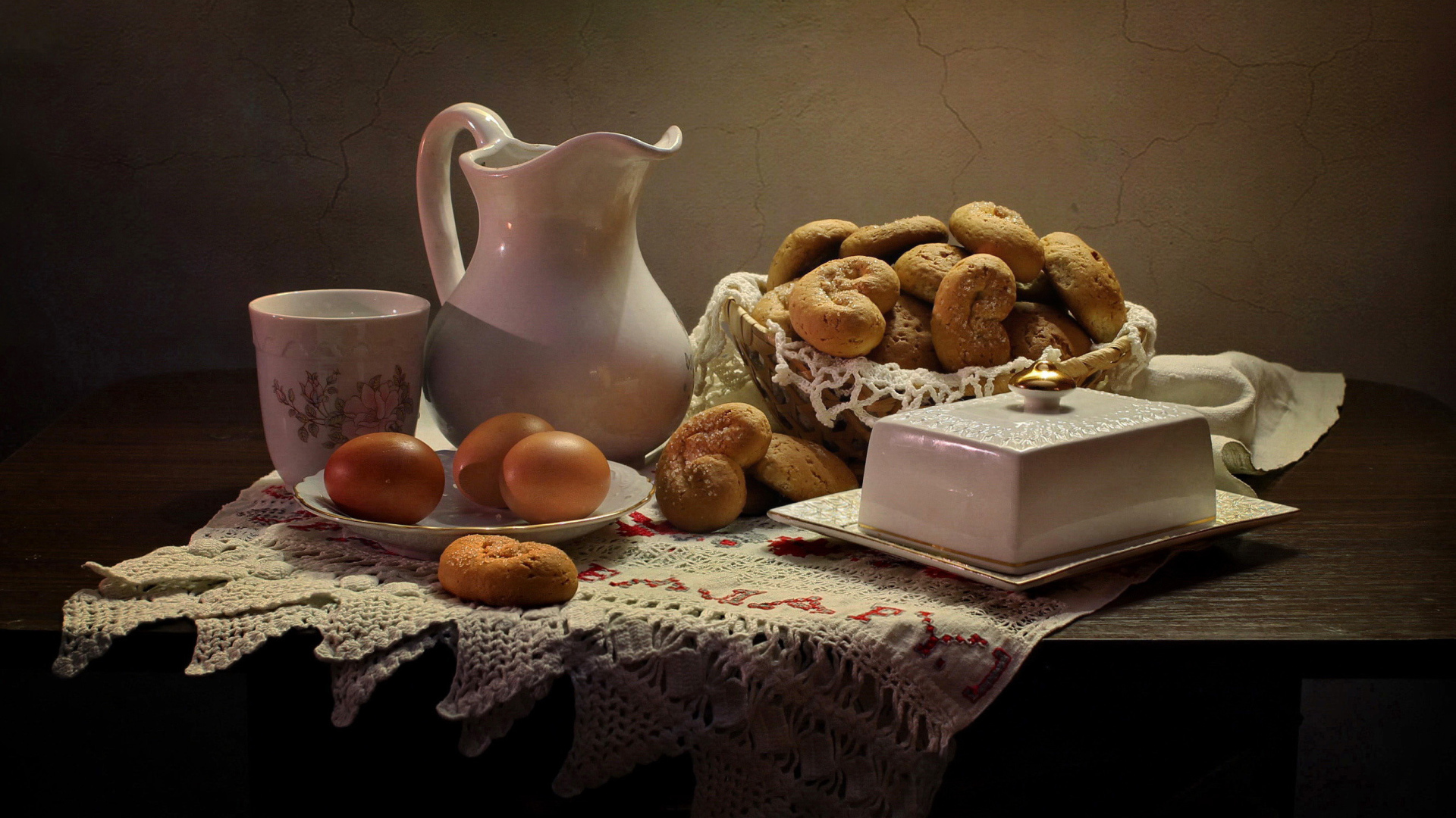 Вареные яйца на столе с кувшином, выпечкой и масленкой 