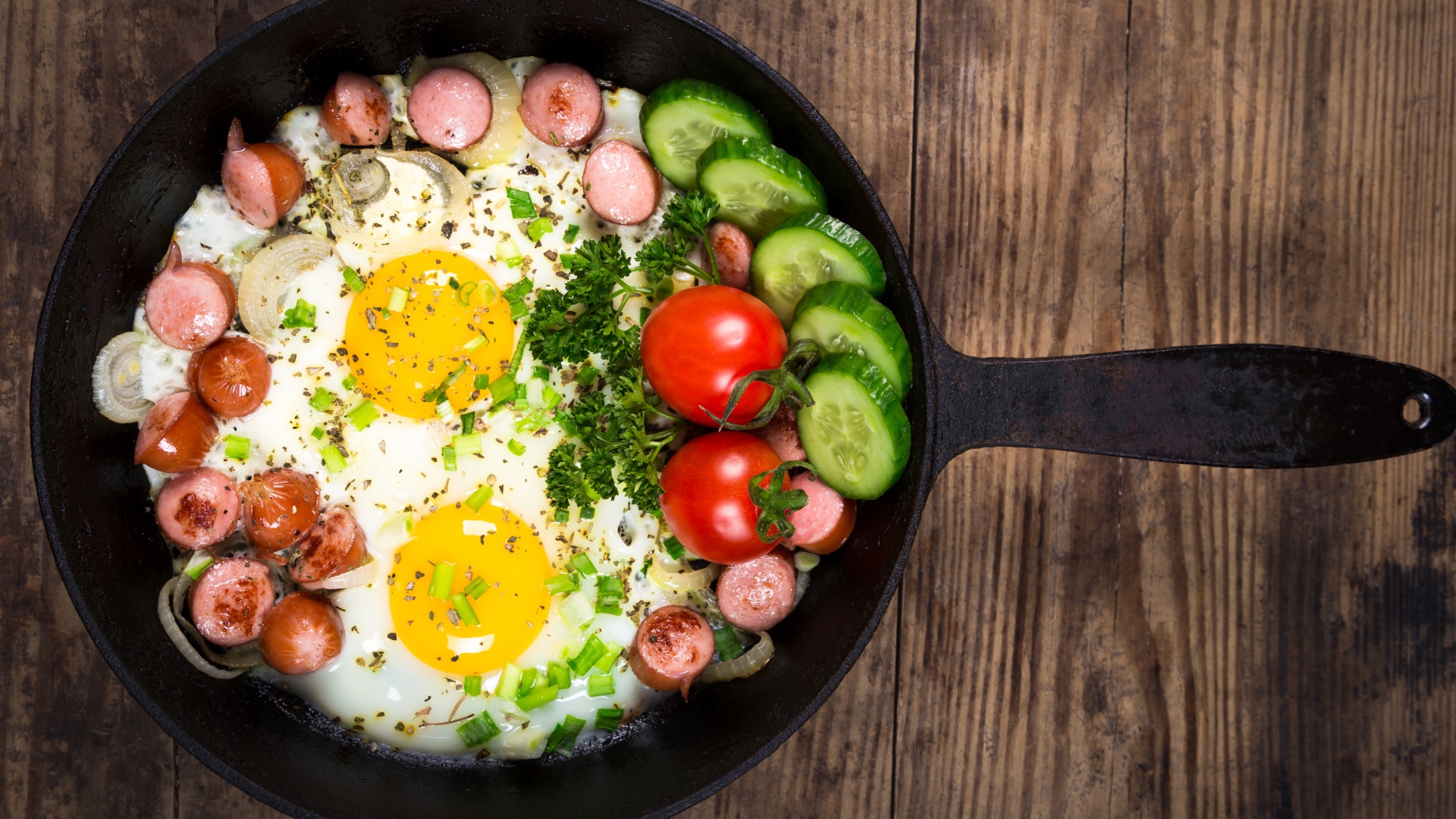 Яичница в сковороде с овощами и кусочками сосиски