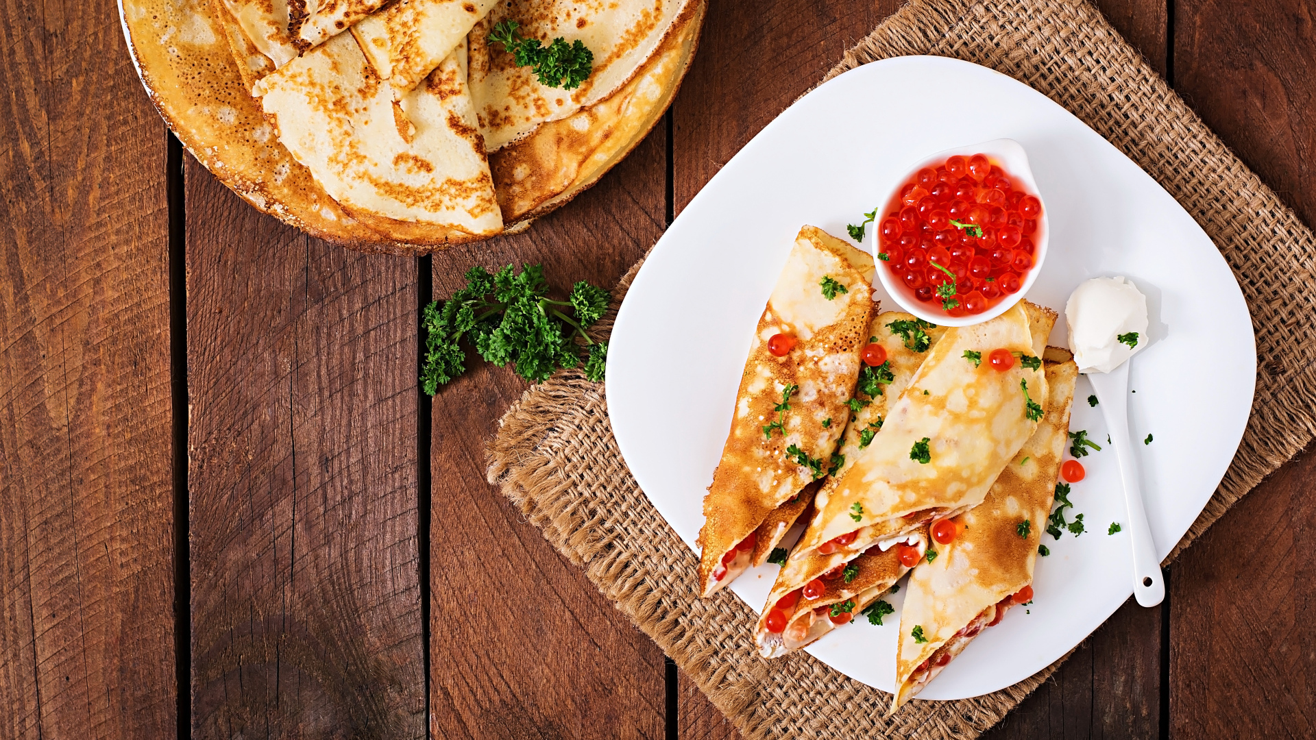 Рулетики из блинов на белой тарелке с красной икрой 