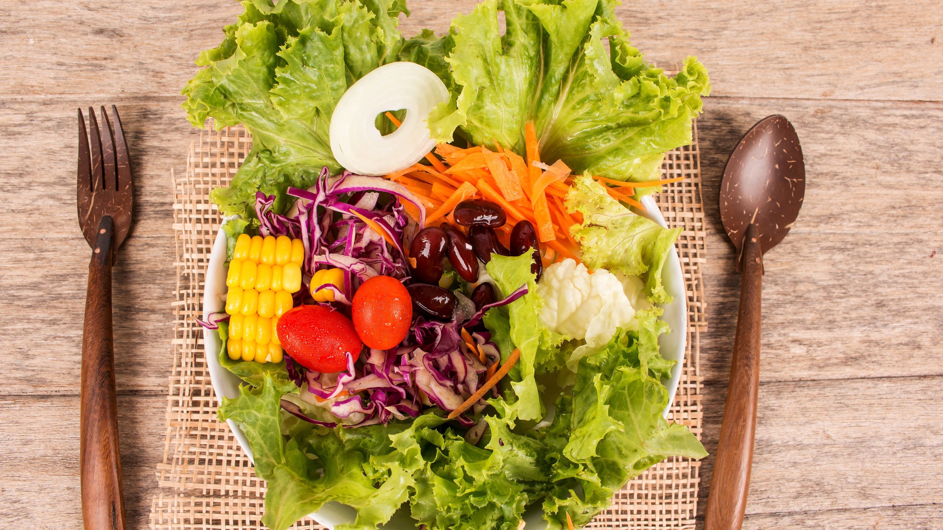 Салат с овощами и зелеными листьями салата в тарелке на столе со столовыми приборами