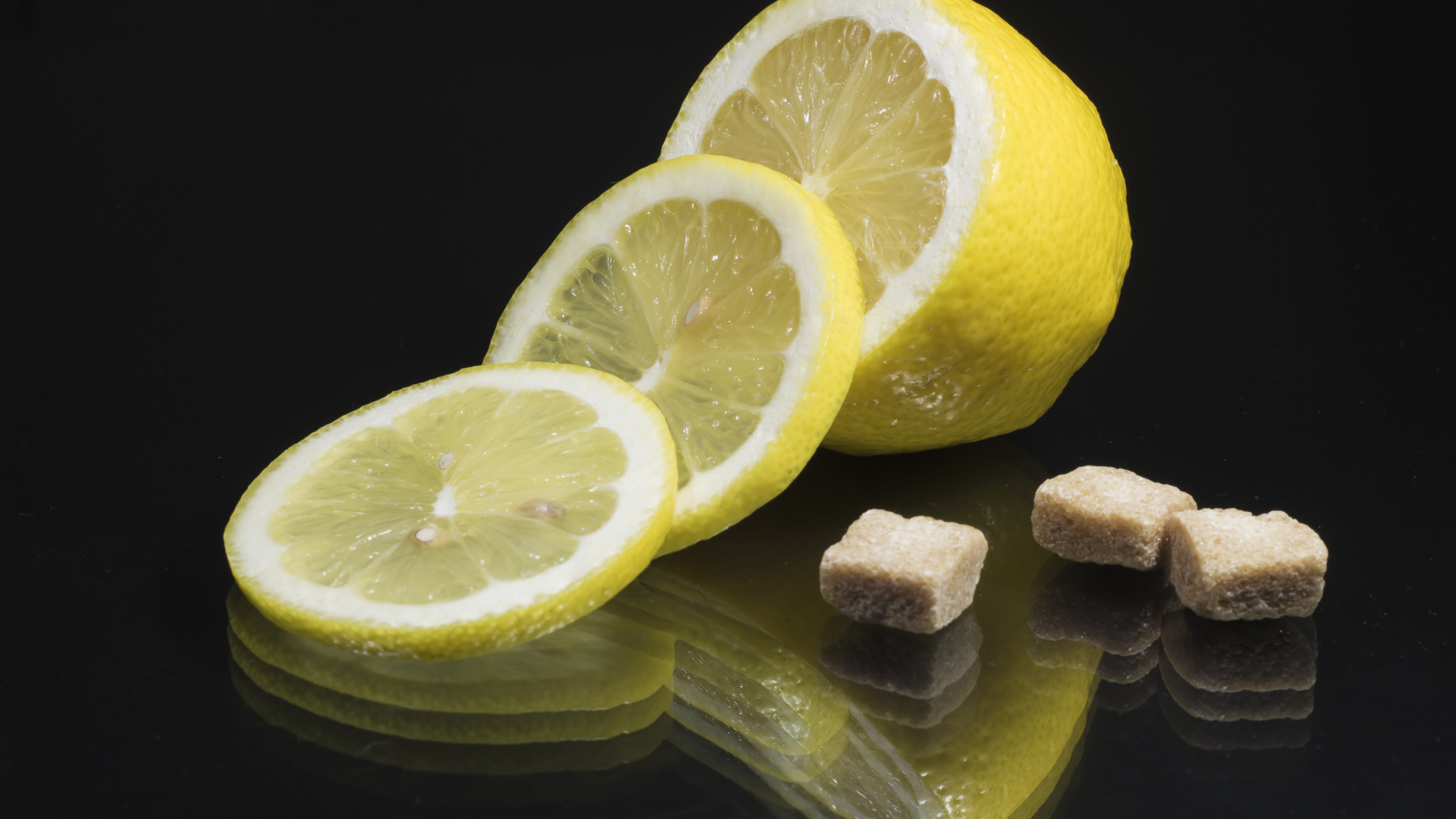 Нарезанный лимон с кусочками коричневого сахара на черном фоне