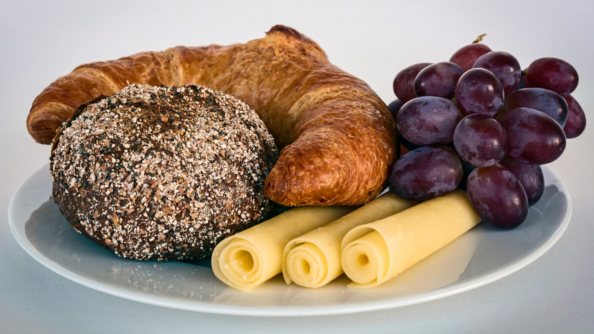 Свежая выпечка с сыром и розовым виноградом на белой тарелке 