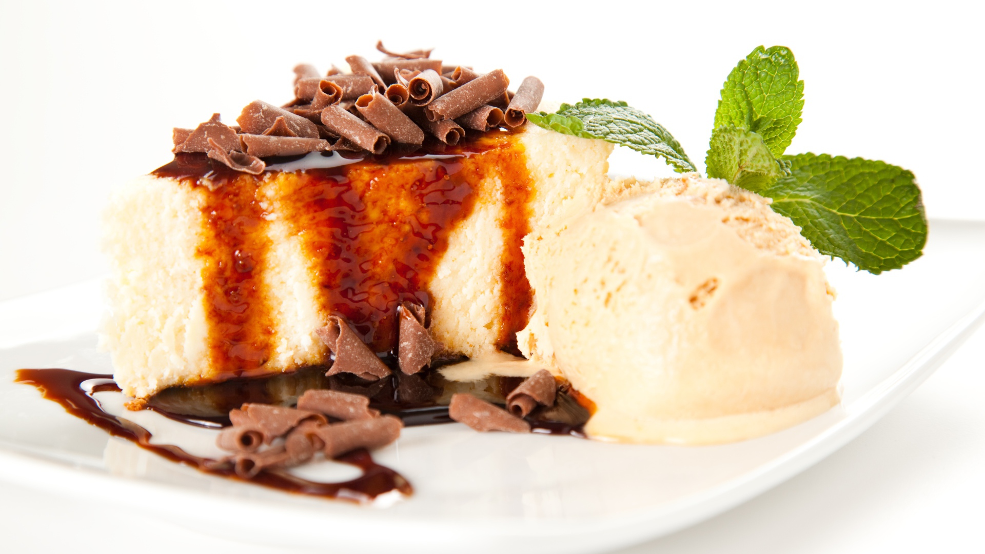 Кусок чизкейка с шоколадом и шариком мороженого на белой тарелке 