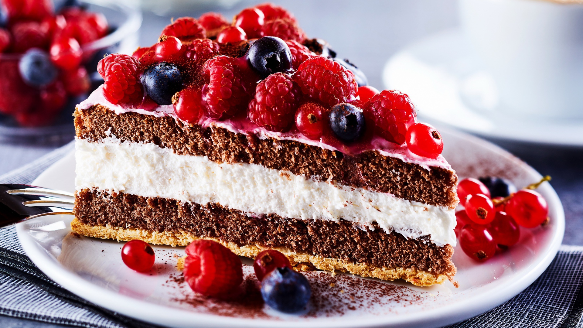 Аппетитный кусок торта на тарелке с ягодами малины, красной смородины и черники