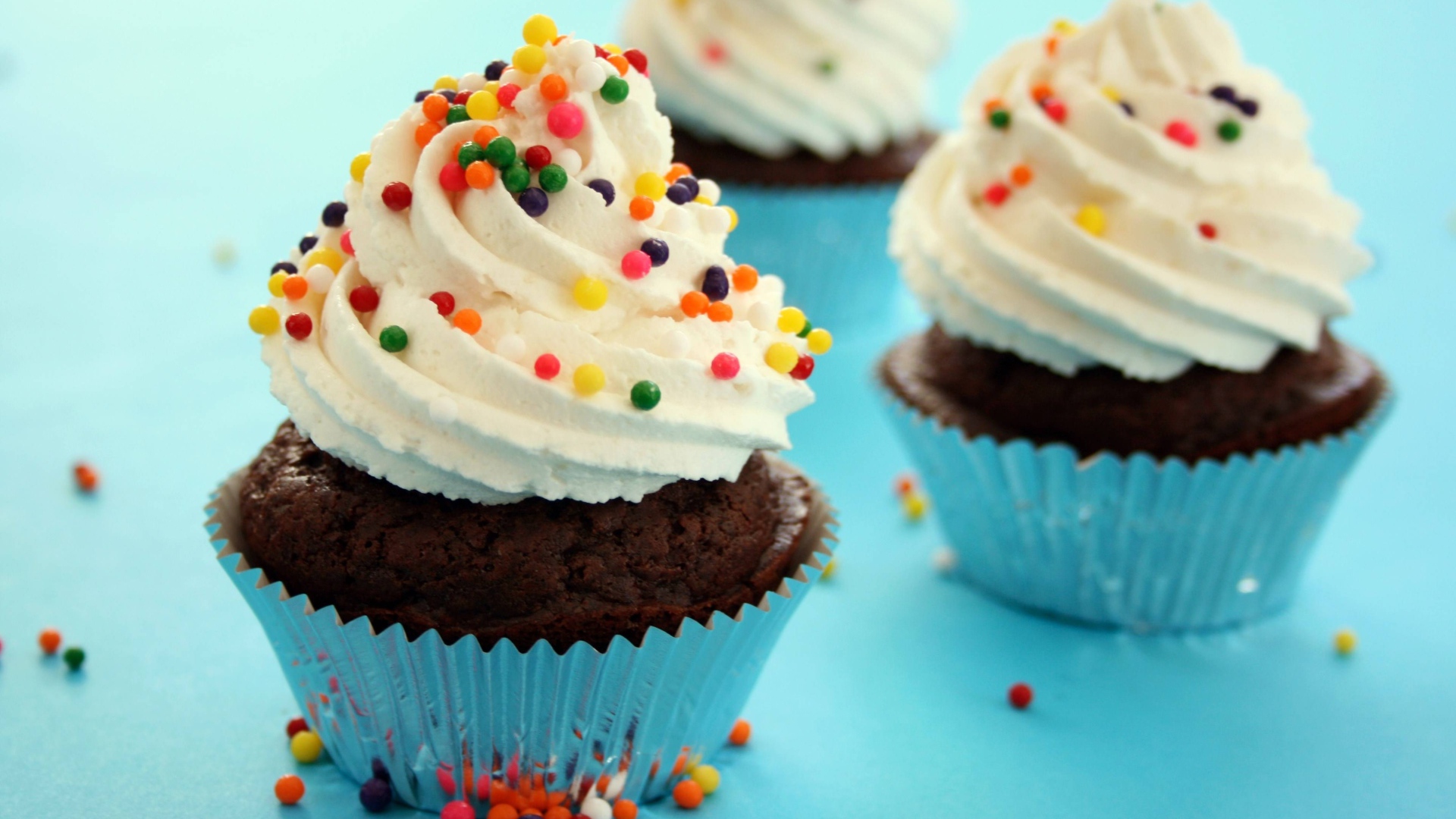 Шоколадные кексы со сливками и цветными брызгами на голубом фоне