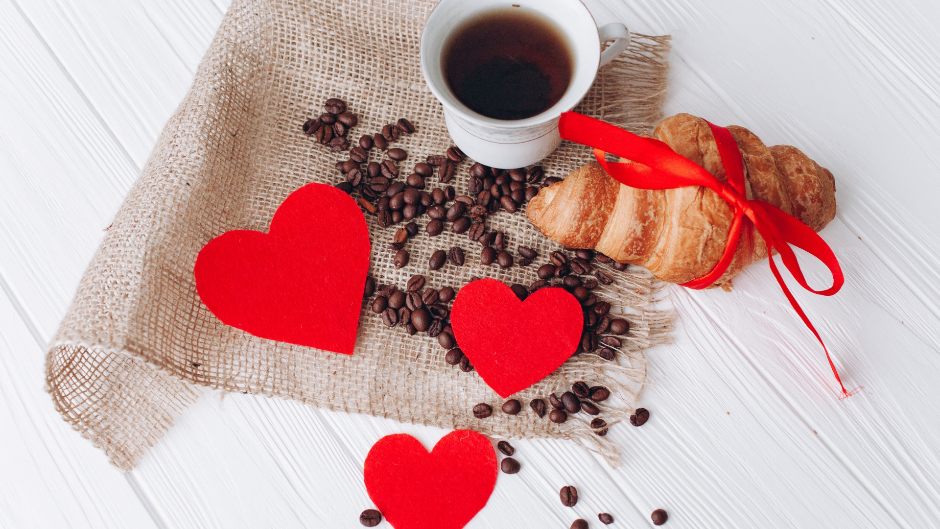 Круассан с чашкой кофе и кофейными зернами на столе с красными сердечками