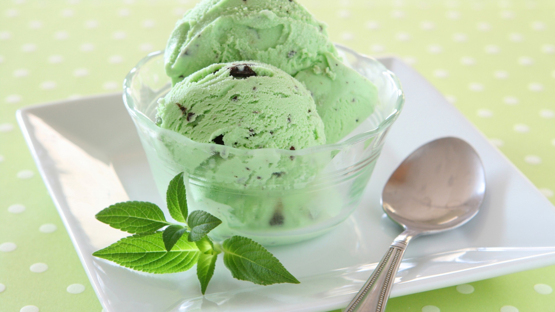 Зеленые шарики мороженого с шоколадом и мятой на тарелке с ложкой