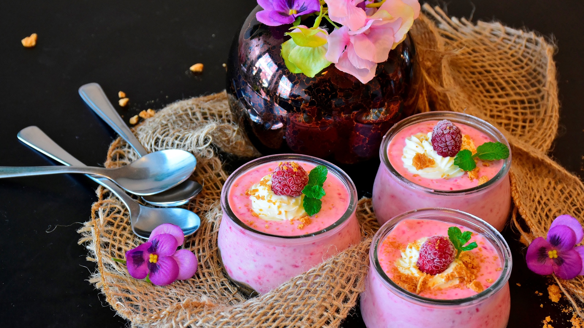 Три банки десерта с малиной на столе с цветами