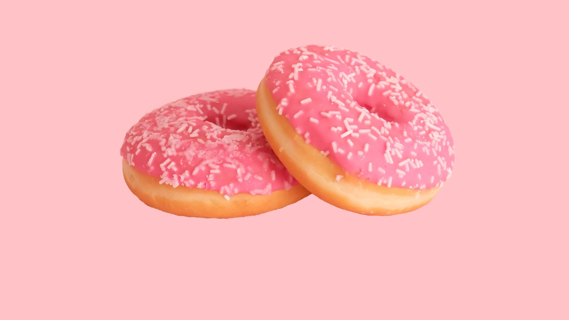 Два пончика с глазурью на розовом фоне