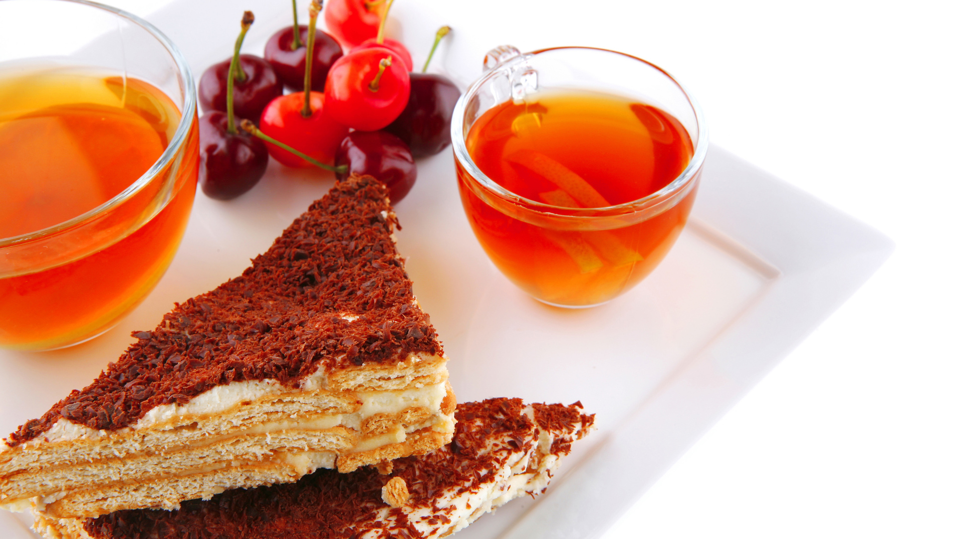 Два кусочка пирожного на столе с чаем и вишнями на белом фоне