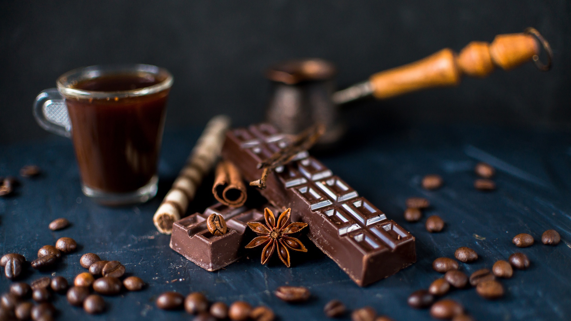 A cup of coffee on a table with chocolate and coffee beans